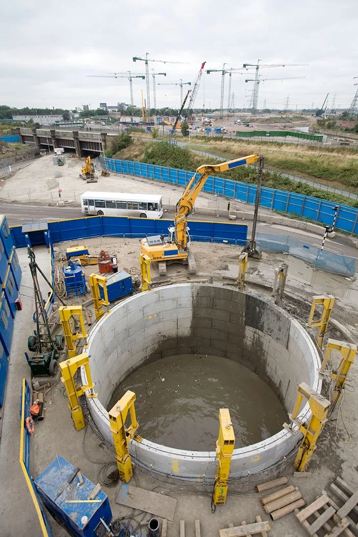 A arial view of the Pudding Mill Pumping Station construction site with large circular manhole being assembled, yellow machinery, construction workers, and cranes in the background.