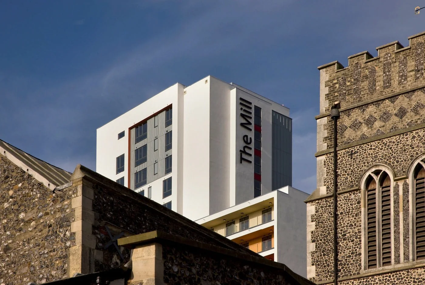 A modern white high-rise building with the sign 'The MIXX' on its side, viewed above older stone buildings in an urban setting.