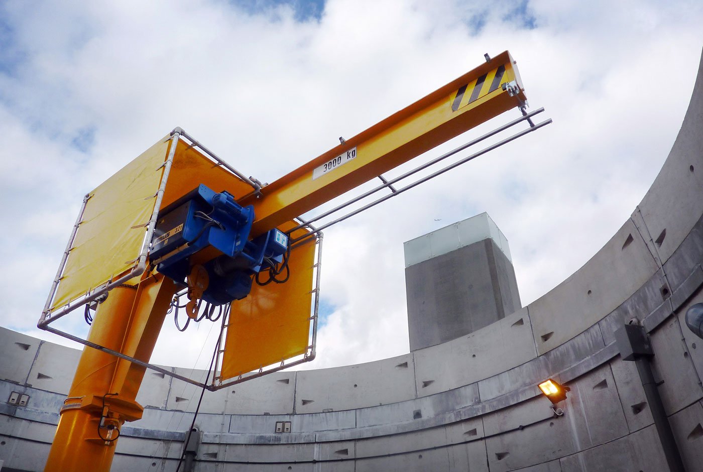 A construction crane lifting materials inside a circular concrete structure with a tall building in the background.