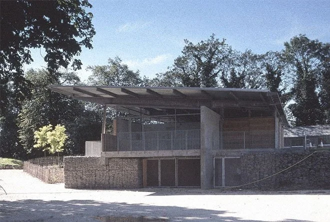 Crystal Palace Park Renovation with a large roof, surrounded by trees and a stone wall, with a gravel area in the foreground.