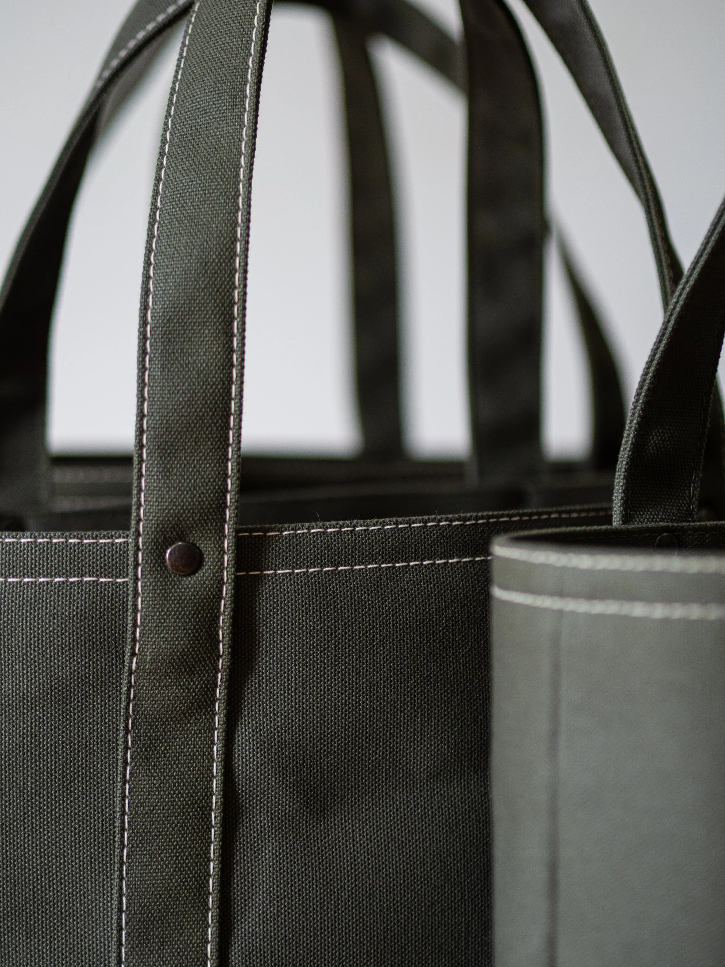 A close-up of a tote bag with contrast stitching and rivits