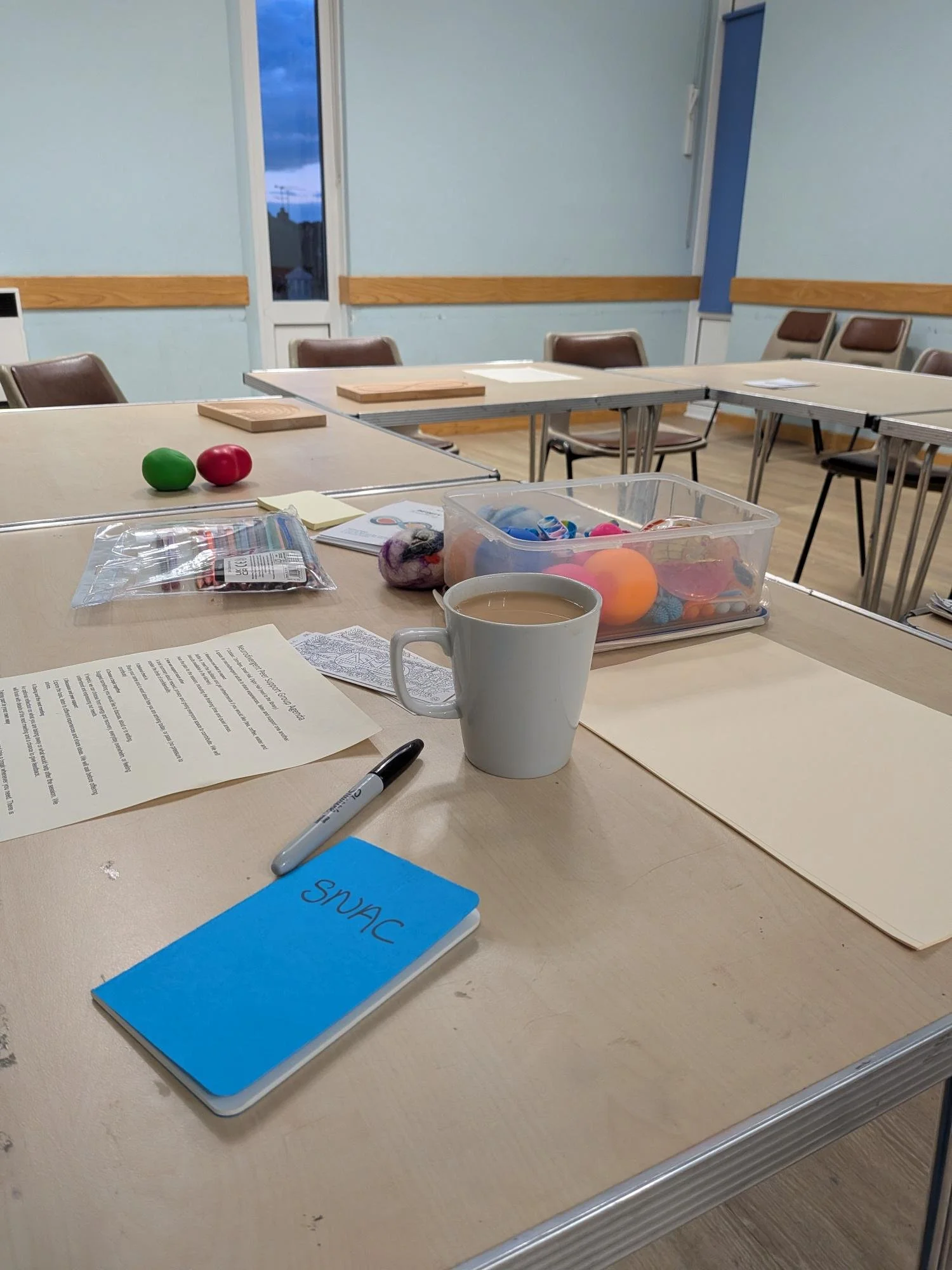 A mug of tea, a box of fidget toys, a notebook on a table at the Digby Hall just before welcoming people into the peer support group