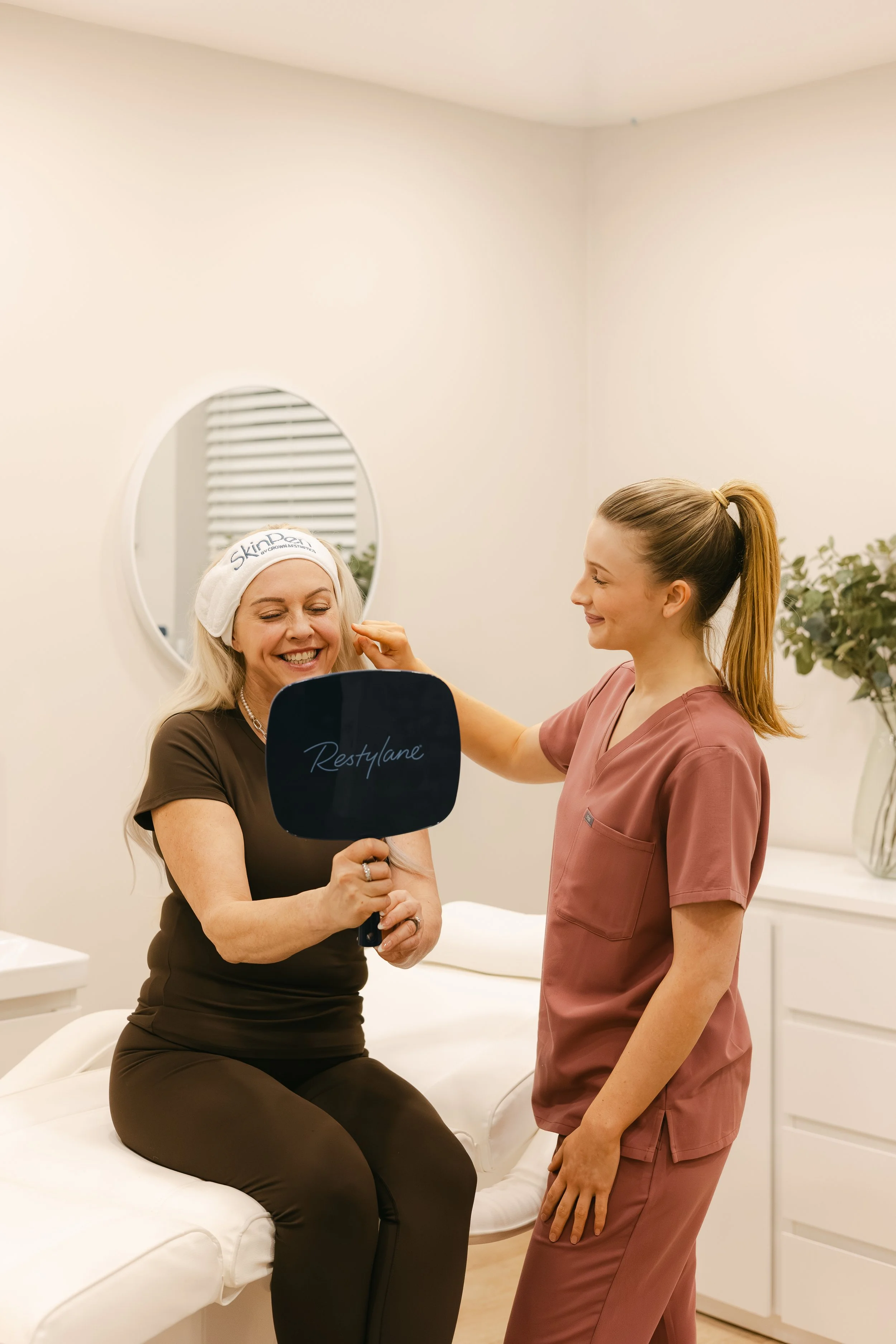 Skinpen treatment being undertaken at a doctor lead aesthetics practice in Nottingham. Two women in the clinic. One looking into a mirror and the practitioner is advising on the treatment.
