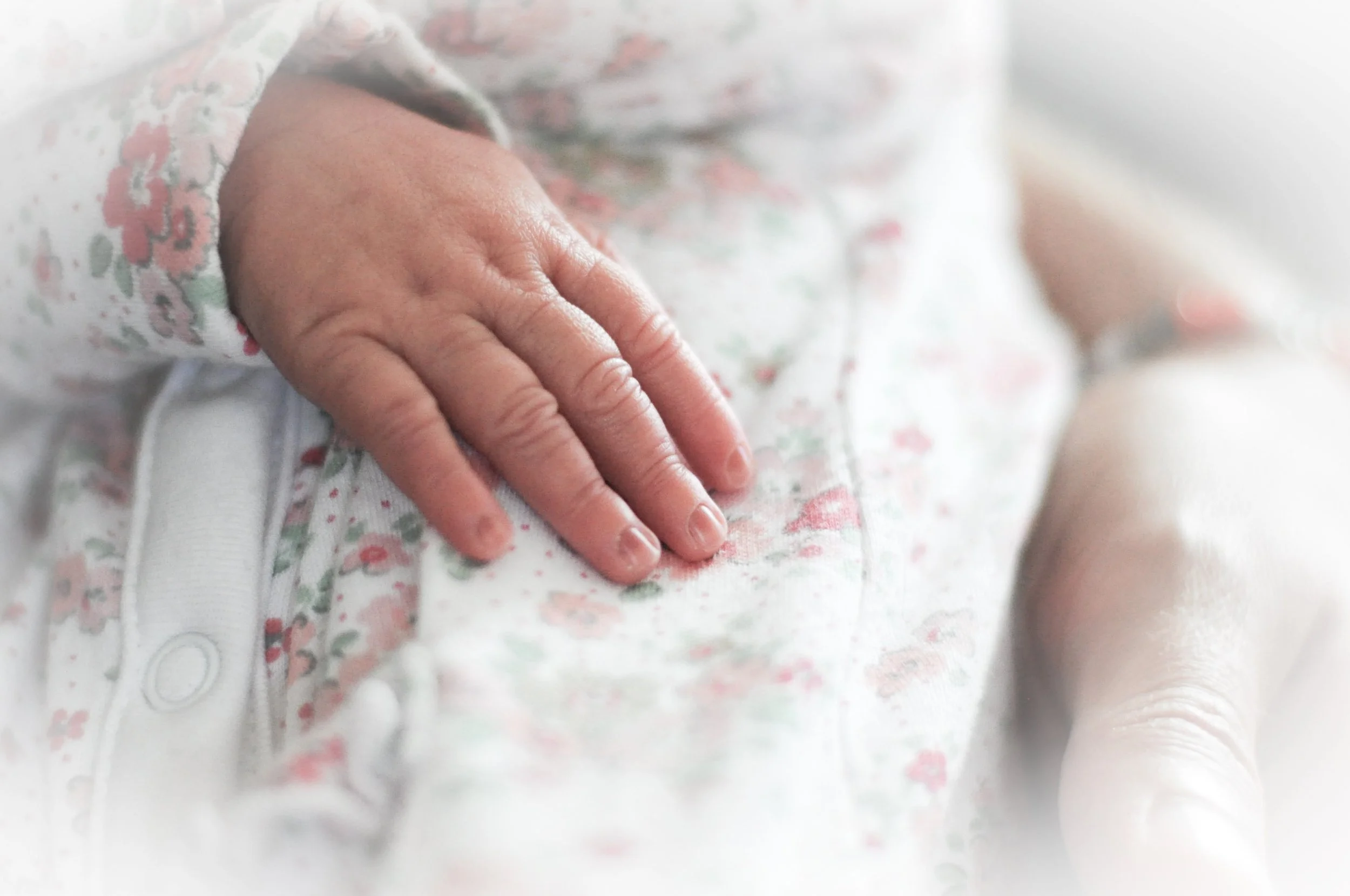 Close-up of a newborn baby's hand resting on a floral-patterned onesie.