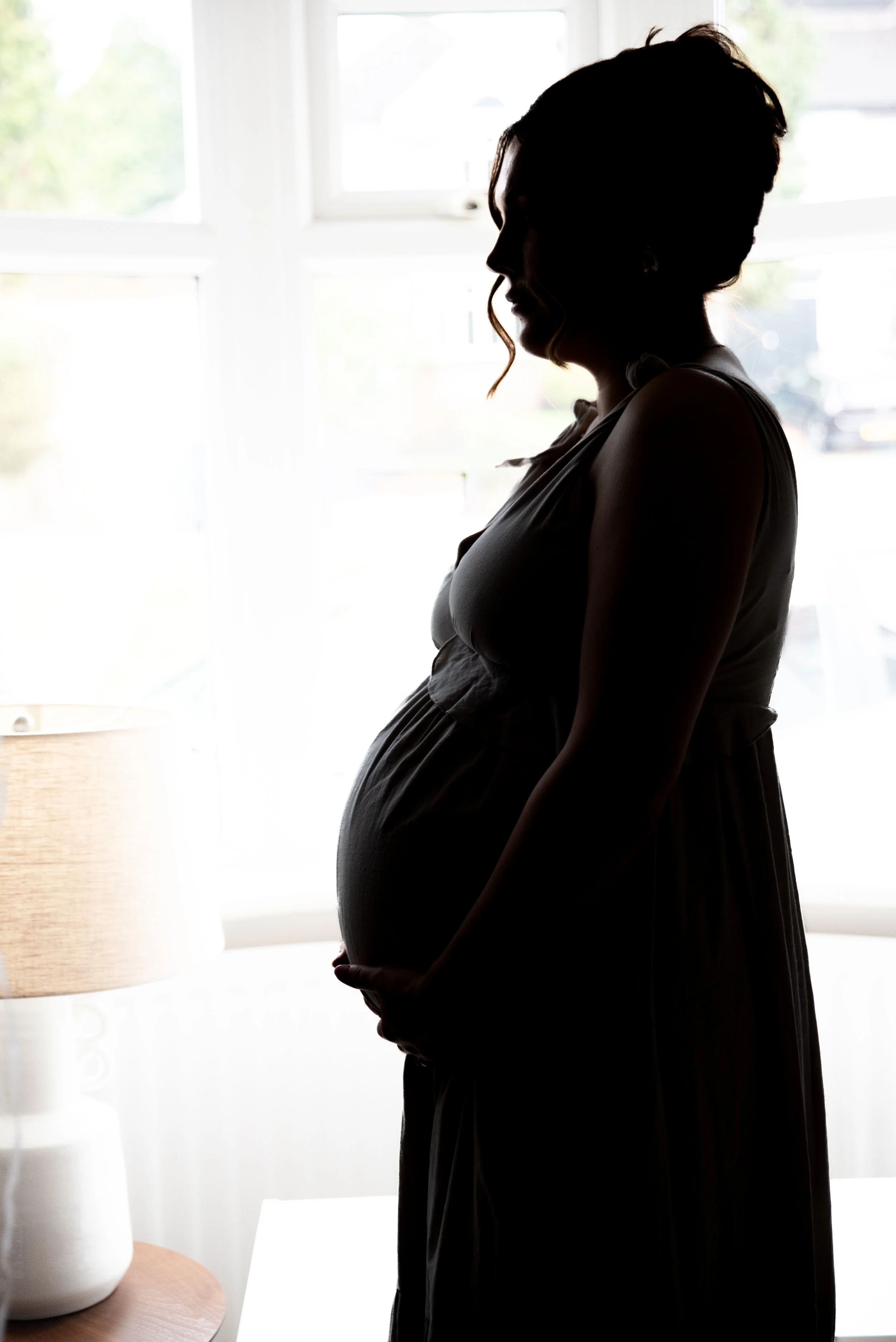 Silhouette of a pregnant woman standing indoors near a window.