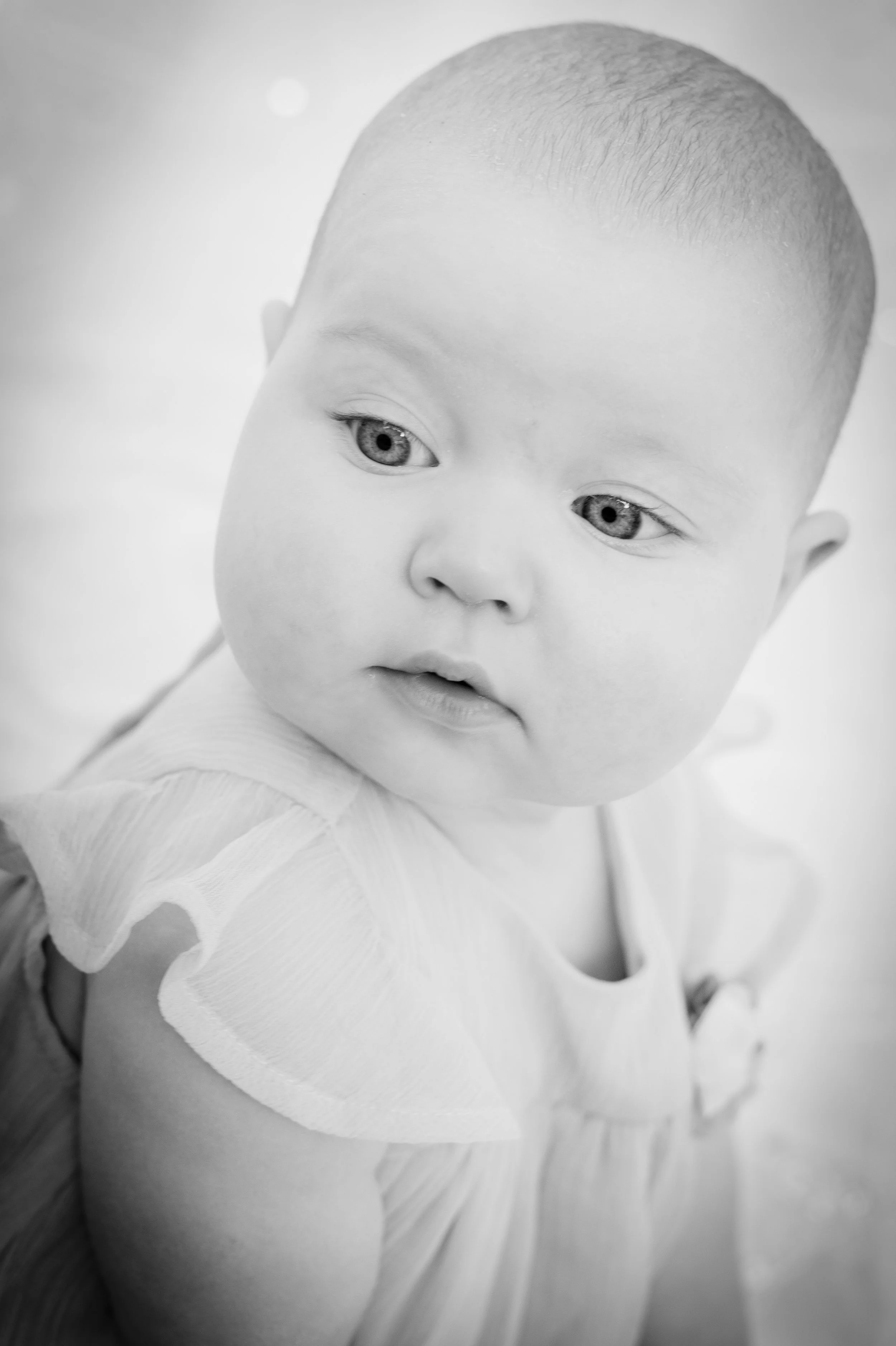 Black-and-white photo of a baby looking to the side, wearing a light-colored dress.