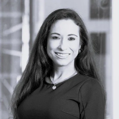 Black and white photo of a man in a suit standing in an office environment.