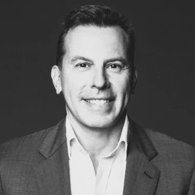 Black and white portrait of a smiling woman outdoors with trees in the background.