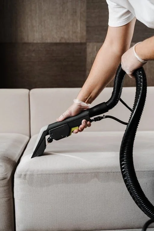 Person cleaning a beige sofa with a handheld vacuum cleaner.