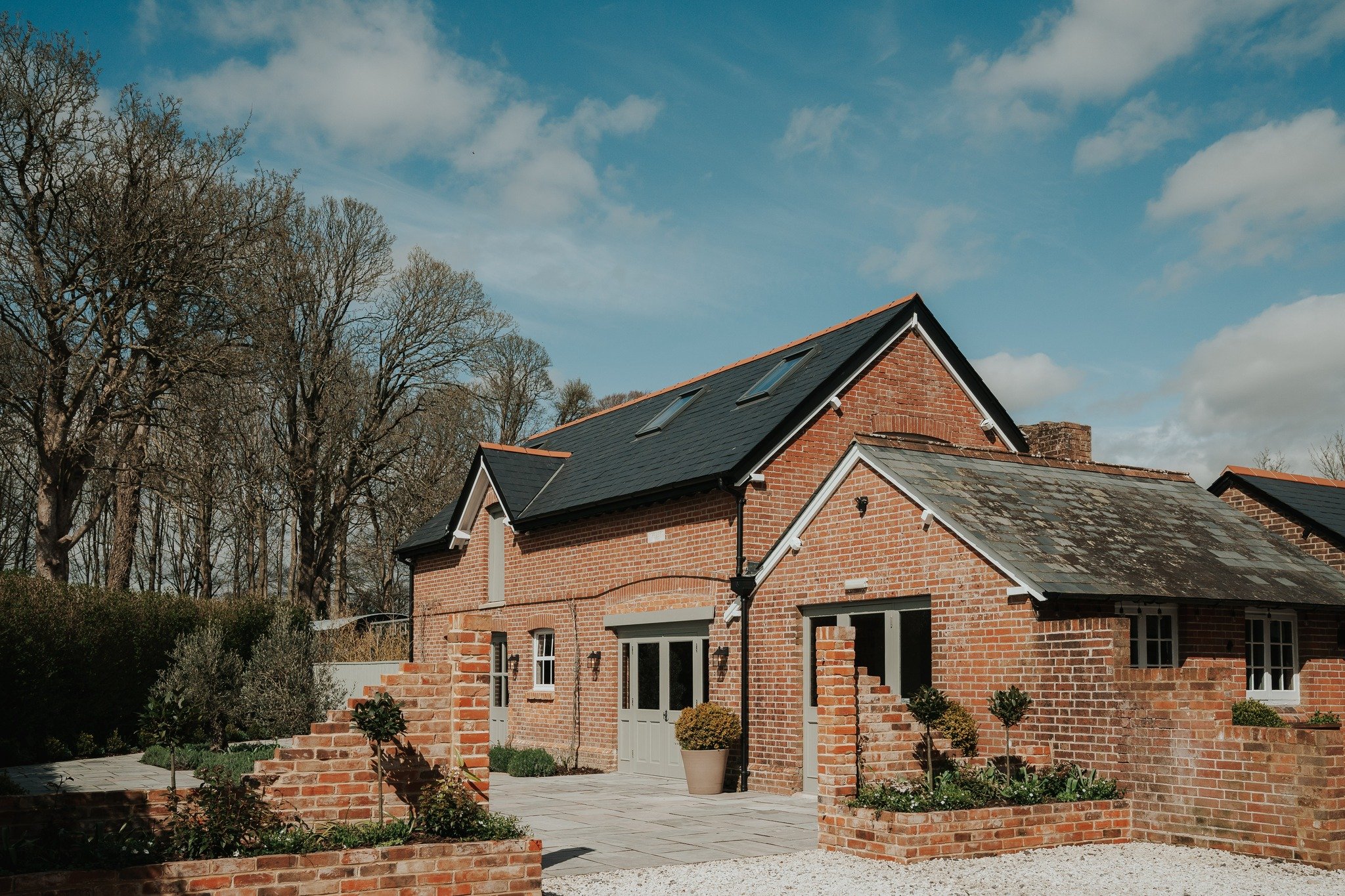 Brick house with tiled roof and garden, trees in the background
