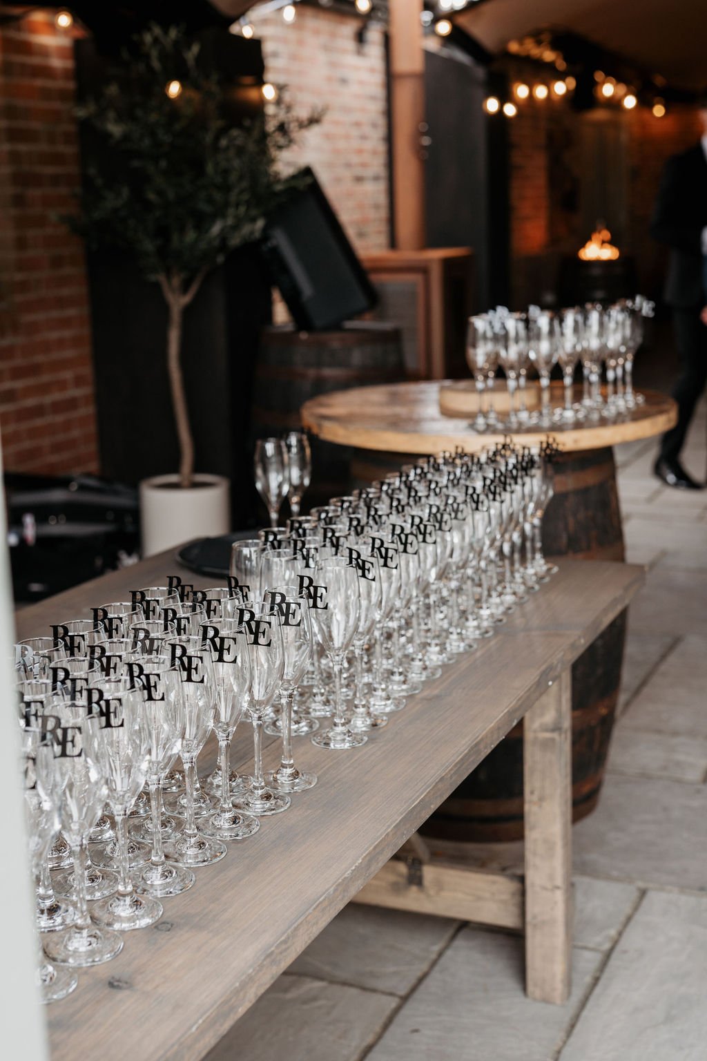 Row of champagne flutes with "RE" logo on a wooden table in a rustic venue.