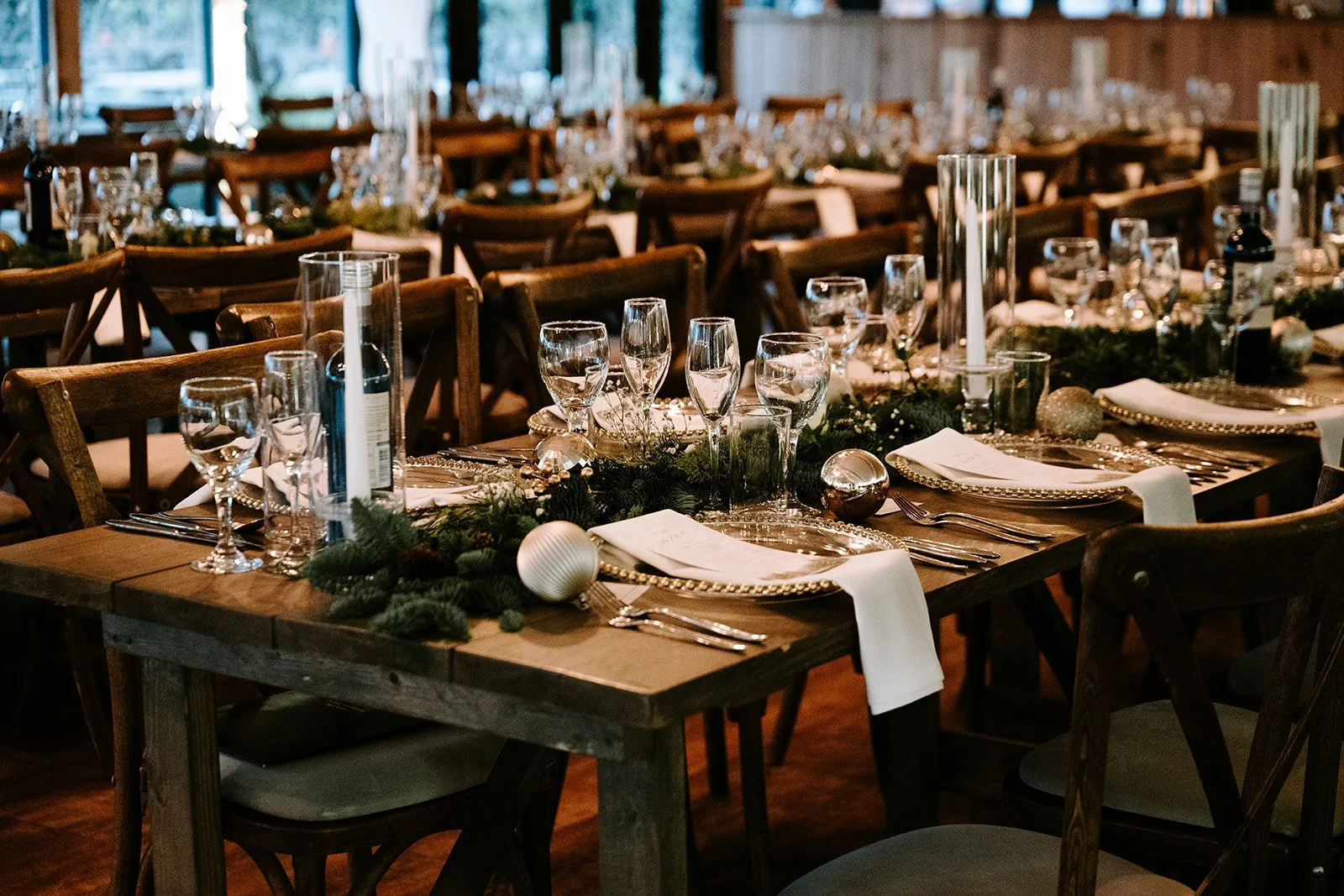 Table set for a festive celebration with glassware, plates, cutlery, and holiday decorations in a rustic wooden venue.