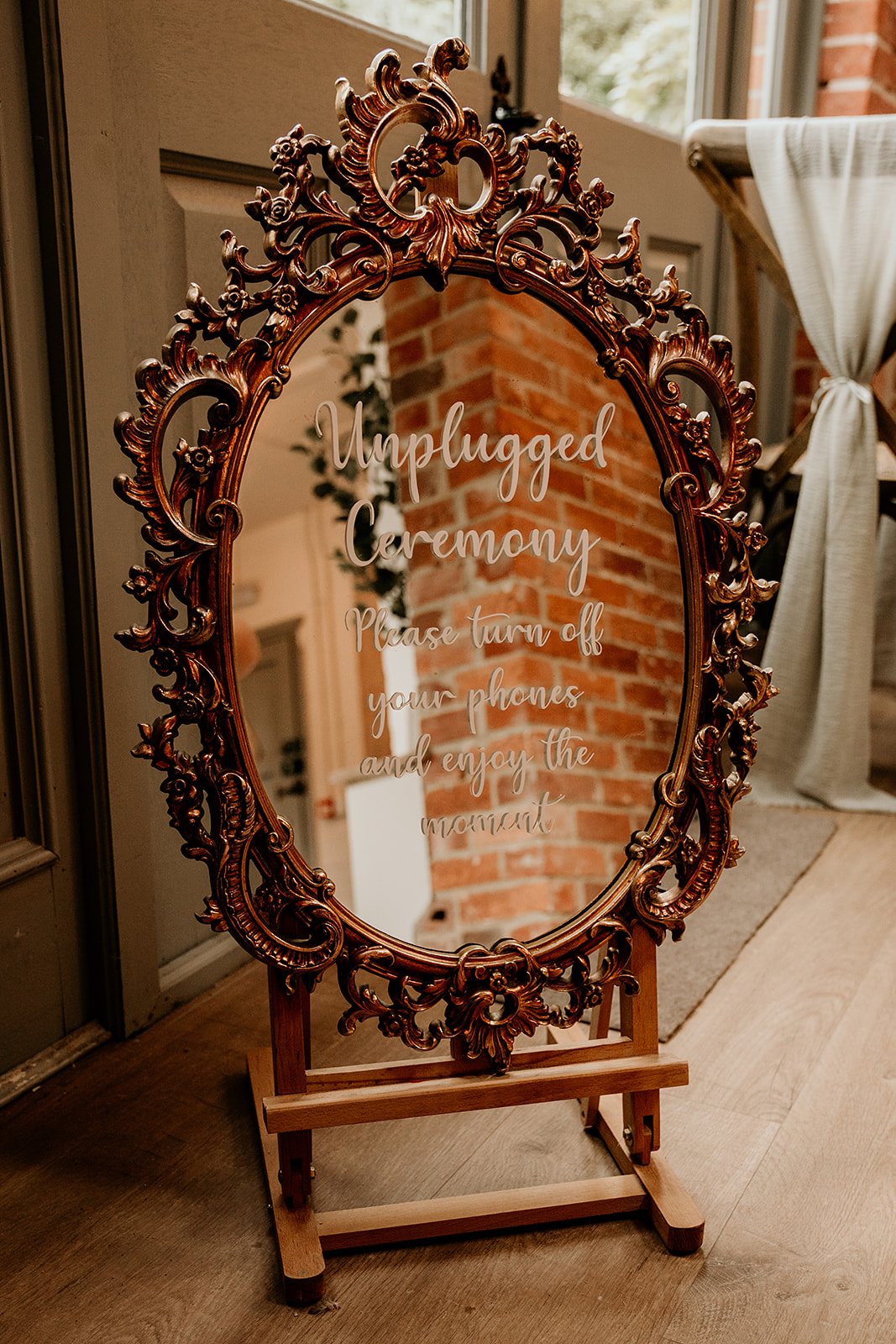 Mirror sign with ornate frame displaying "Unplugged Ceremony, Please turn off your phones and enjoy the moment."