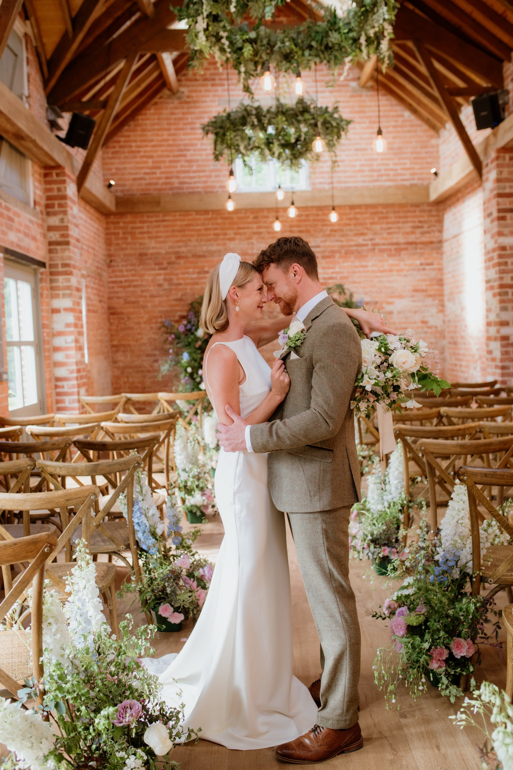Wedding couple embracing in a rustic decorated venue with floral arrangements and wooden chairs.