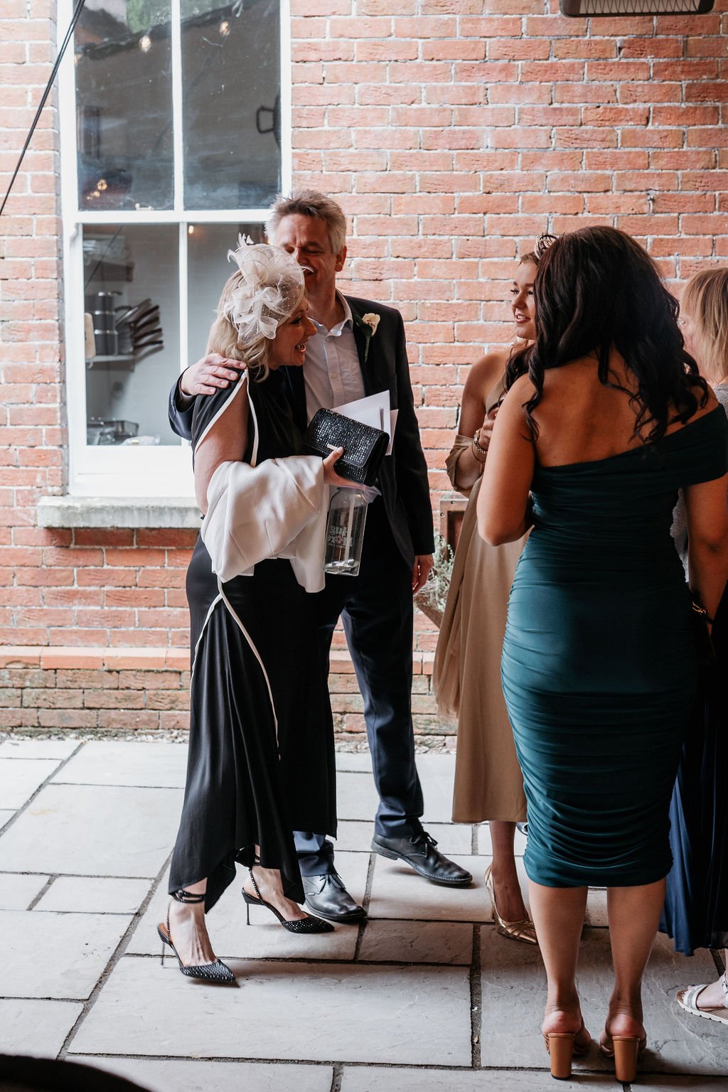 Group of well-dressed people at an event standing outside a brick building, engaged in conversation.