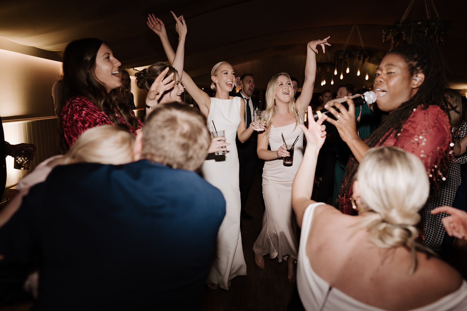 Group of people dancing at a party with a woman singing into a microphone.