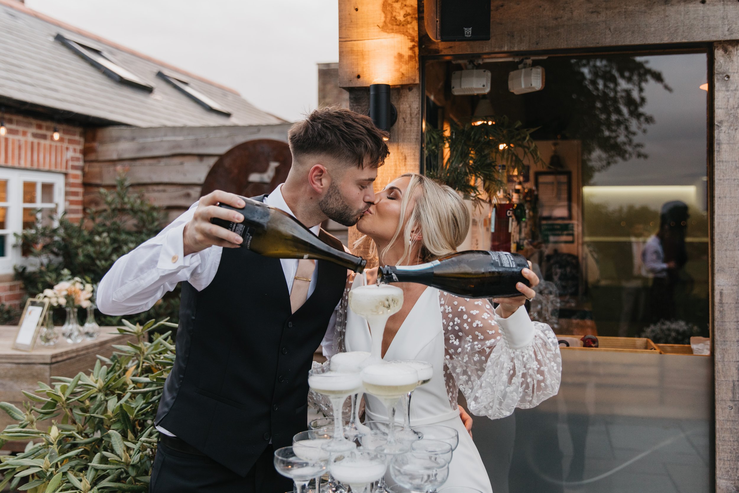 Couple kissing while pouring champagne into glasses tower outdoors