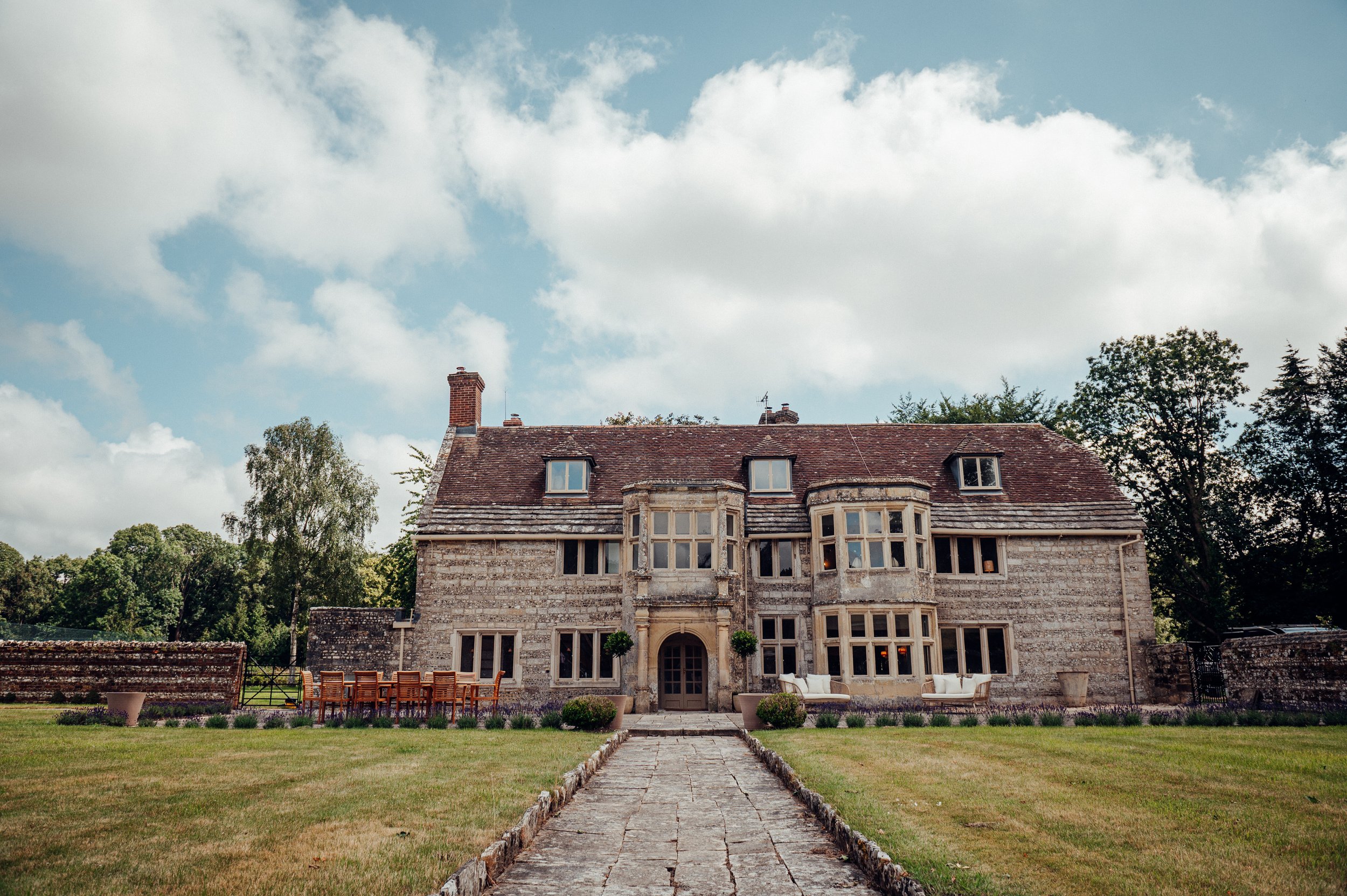 Large stone mansion with multiple windows, surrounded by a lawn and trees, with a pathway leading to the entrance.