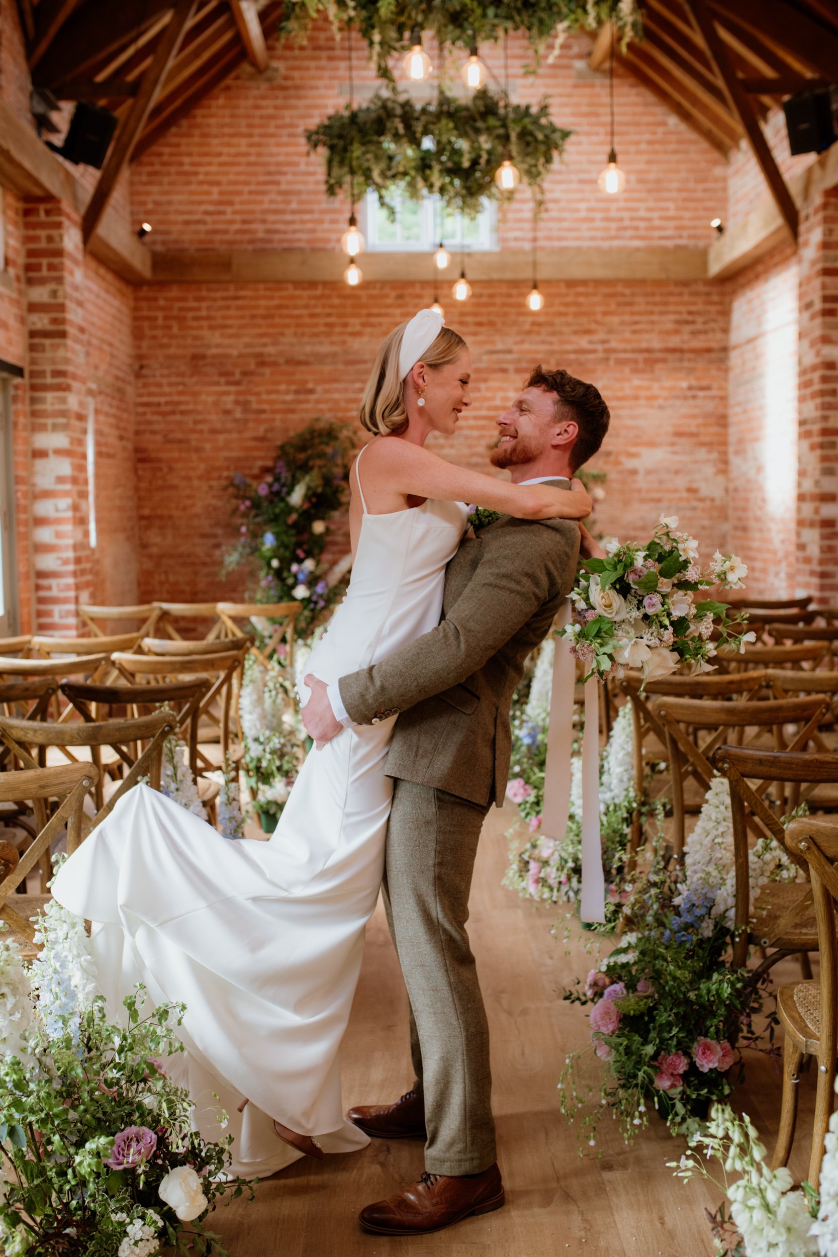 Bride and groom embracing in rustic venue with floral decorations.