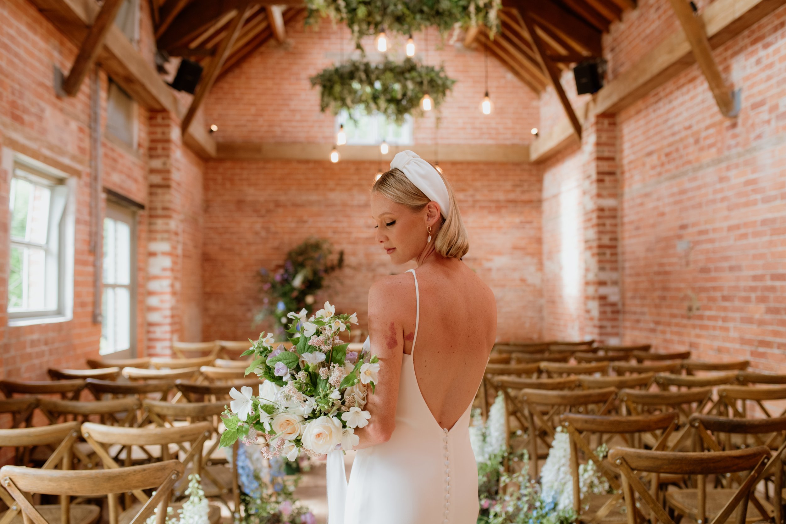 Bride with bouquet in rustic venue with wooden chairs and brick walls
