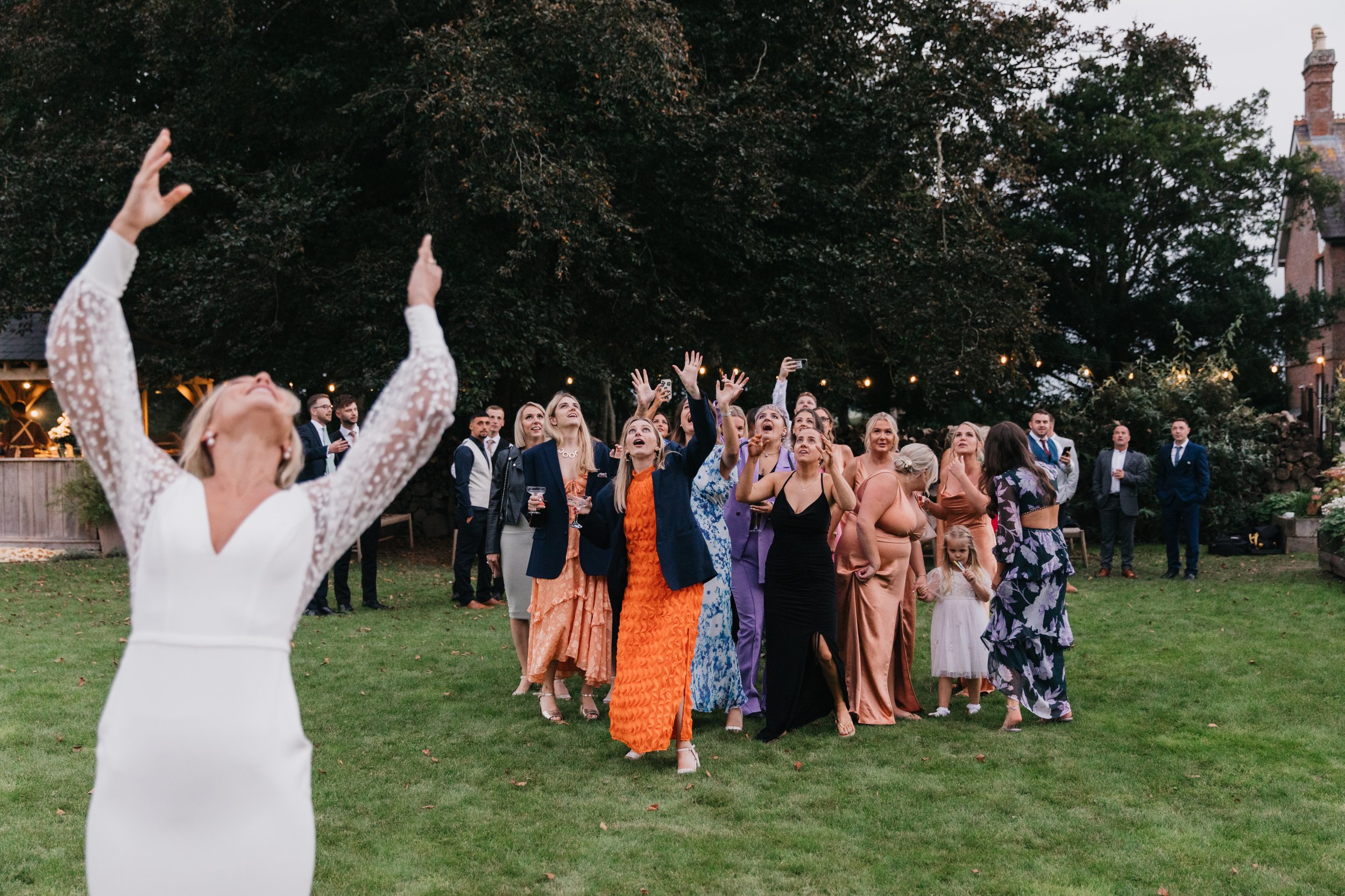 Bride throwing bouquet at wedding, women trying to catch, outdoor setting