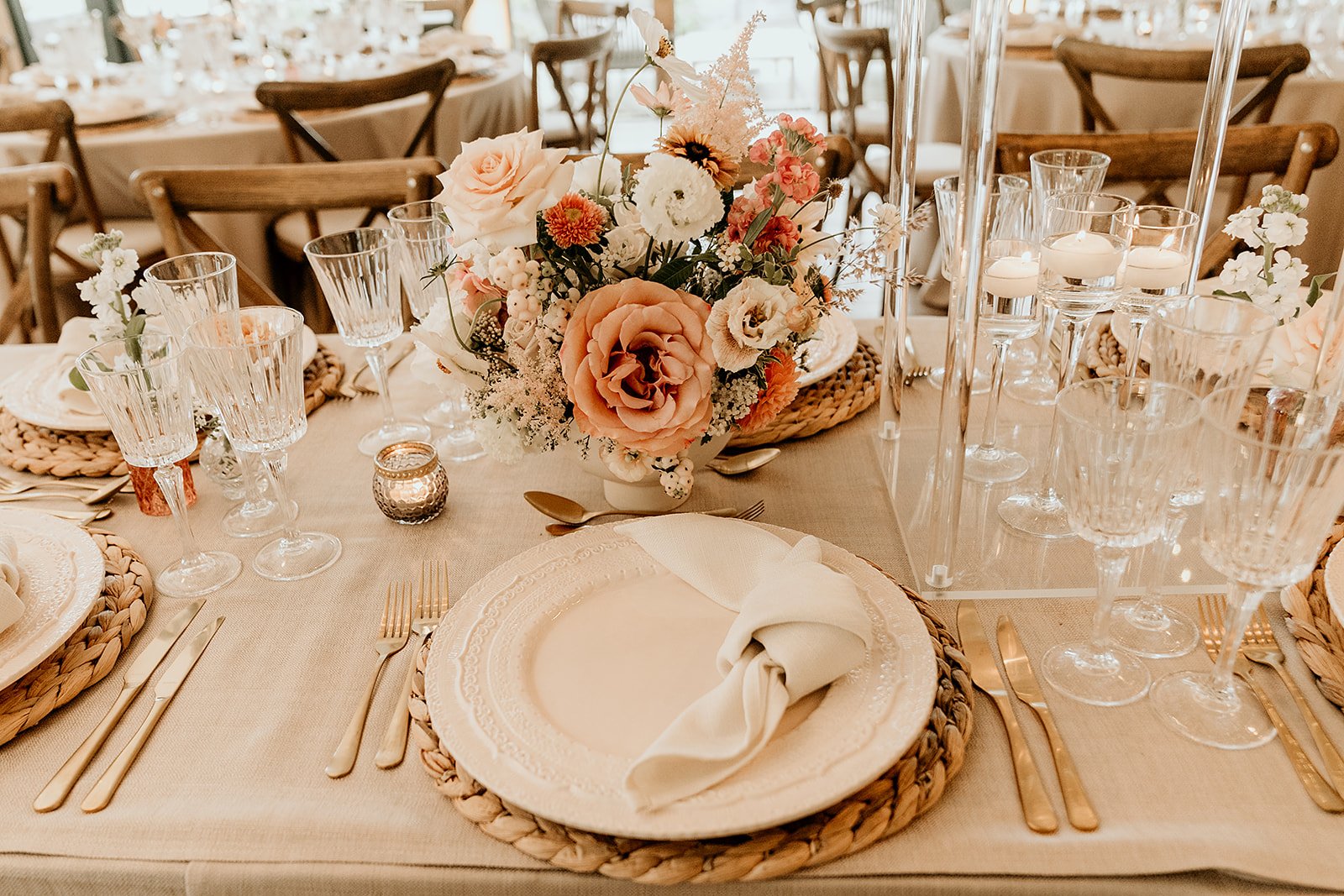 Elegant wedding reception table with floral centerpiece, crystal glassware, gold cutlery, and woven placemats.