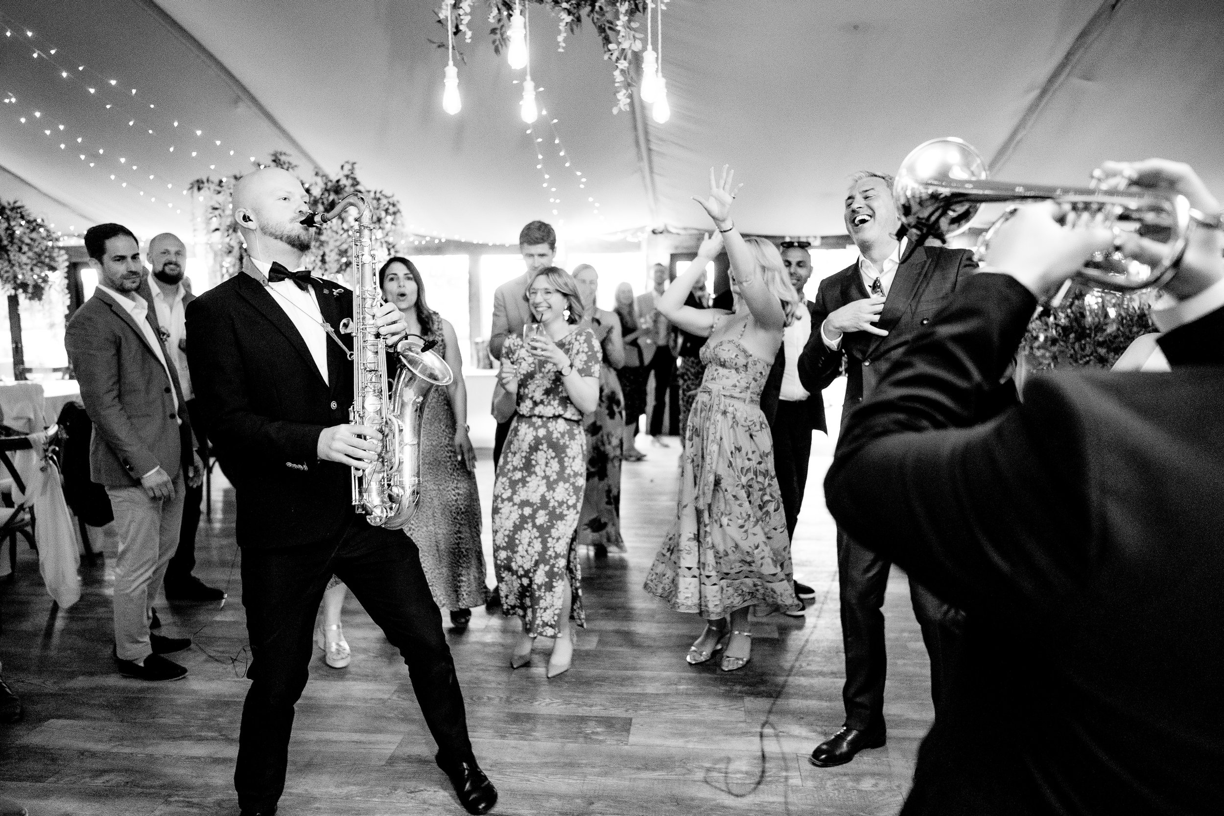 People dancing and enjoying music at a wedding reception, with a saxophonist and a trumpet player performing.