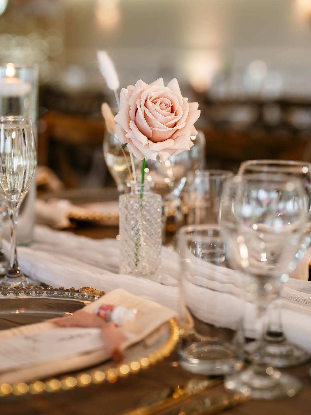 Close-up of a pink rose in a crystal vase on a dining table set for a formal event.