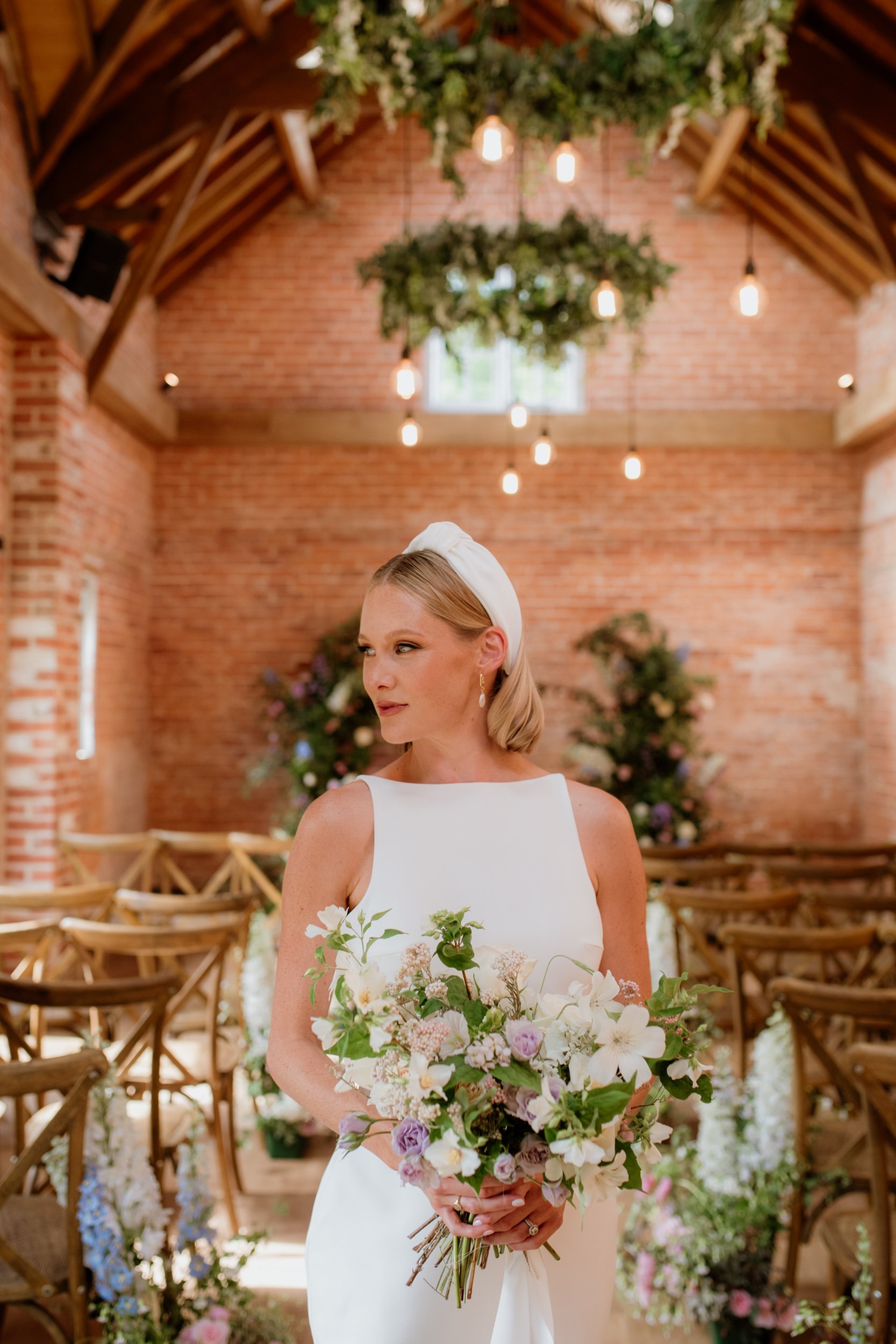 Bride holding bouquet in rustic wedding venue with exposed brick and wooden ceiling.