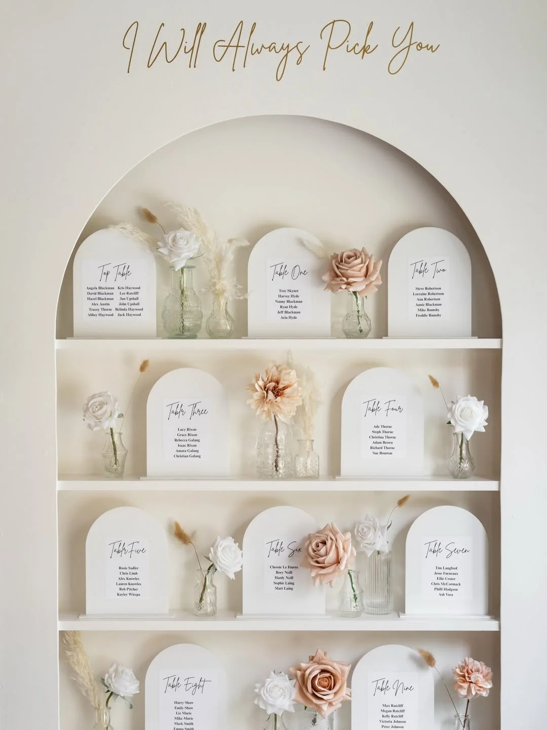 Seating chart with table numbers, names of guests, decorative flowers in vases, and a sign at the top reading 'I Will Always Pick You'.