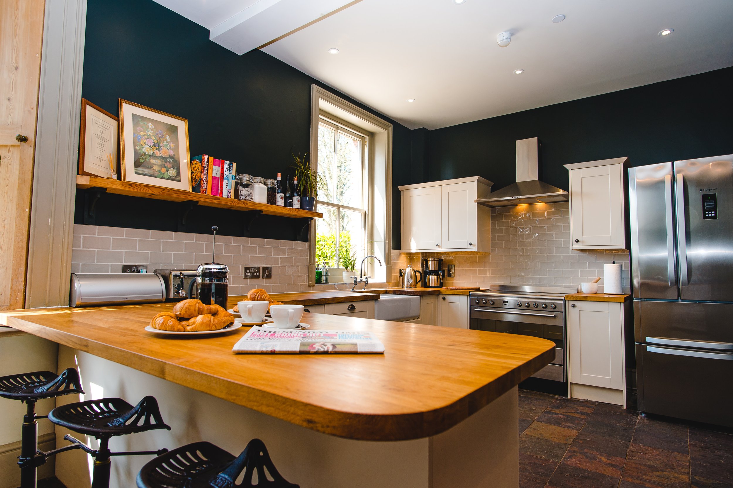 Modern kitchen with wooden countertops, stainless steel appliances, and an island with croissants and coffee cups.