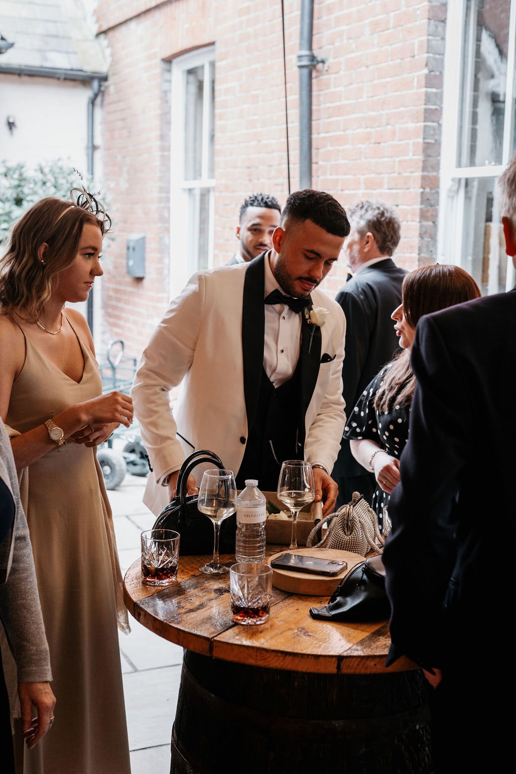People socializing at a formal event, standing around a wooden table with drinks.