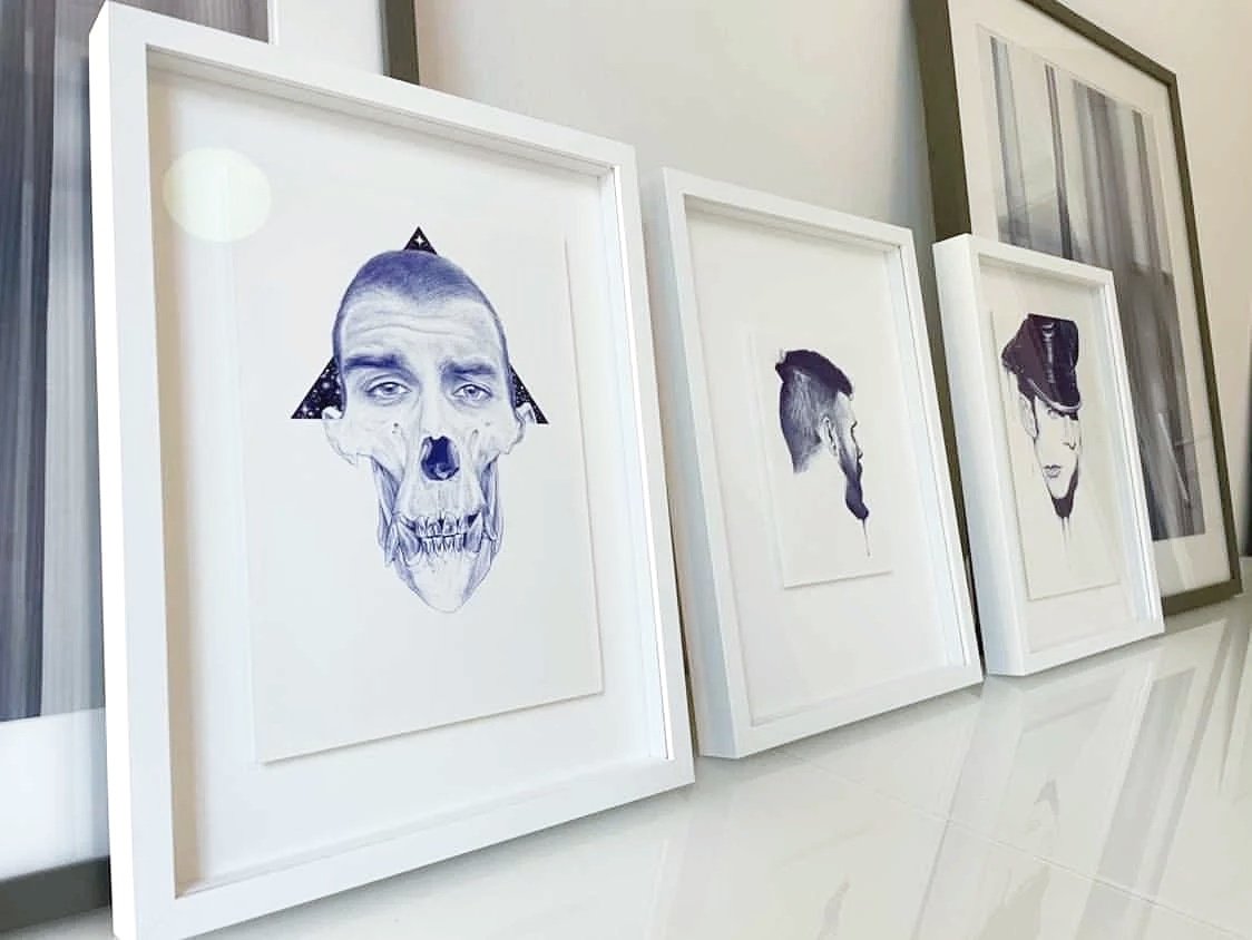 Quatre dessins de portraits de visages, chacun combinant des éléments humains et artistiques, encadrés en blanc, accrochés sur un mur.