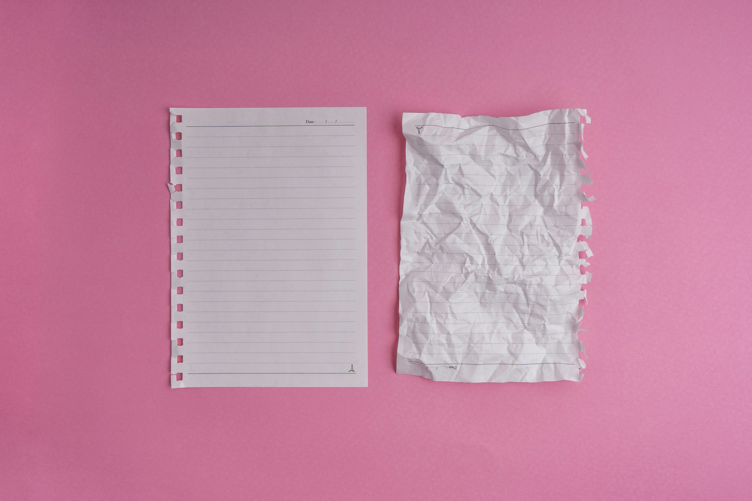 Two sheets of lined paper on a pink background. One is blank and clean, the other has been screwed up and straightened out again