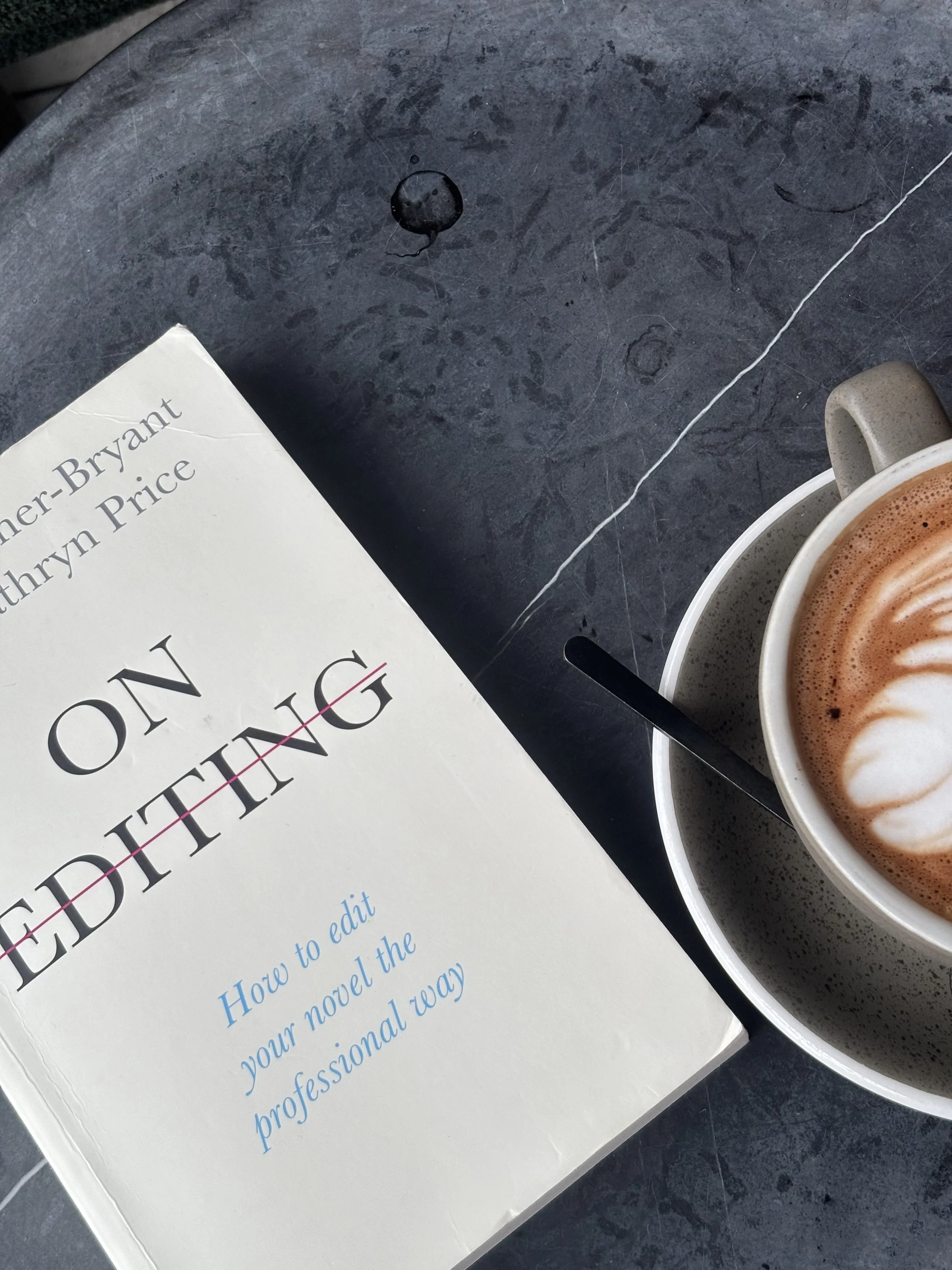 A book titled 'Editing' by Martha A. Seahorn Bryant Price partly visible on a dark, scratched surface, next to a cup of coffee with foam art.