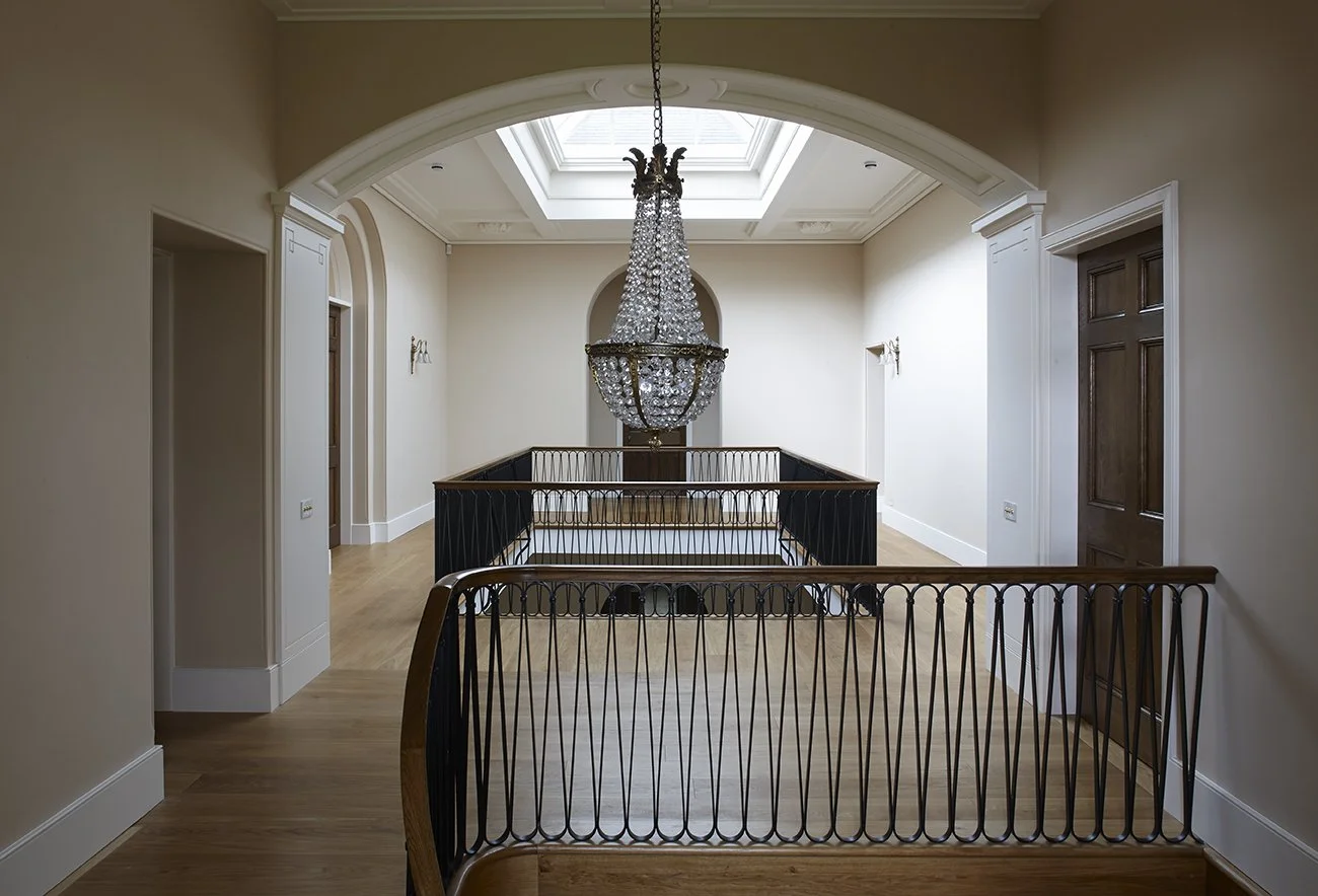 Double-height stair hall with roof lantern, wrought iron balustrade and classical chandelier by Craig Hamilton Architects