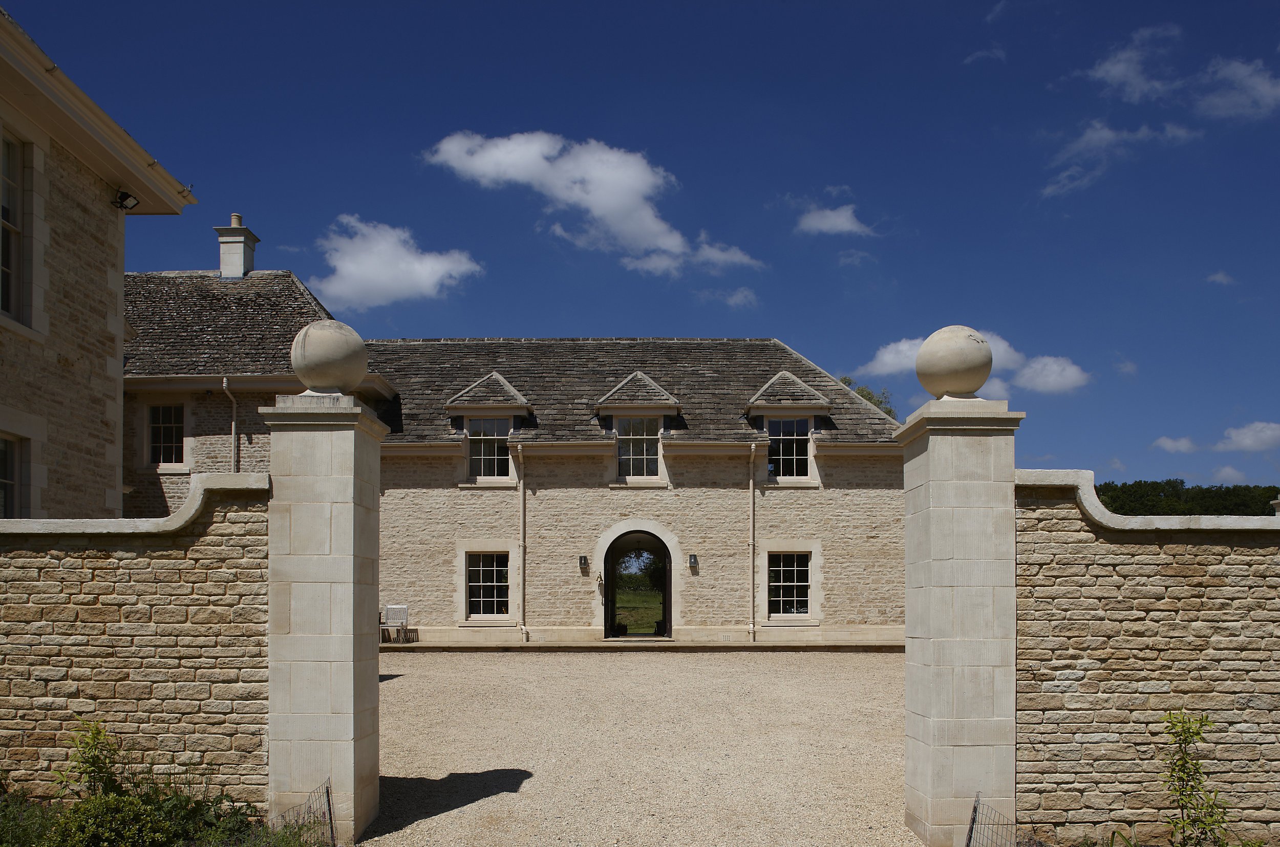 Symmetrical stone entrance court with arched gateway and traditional Cotswolds architecture by Craig Hamilton Architects