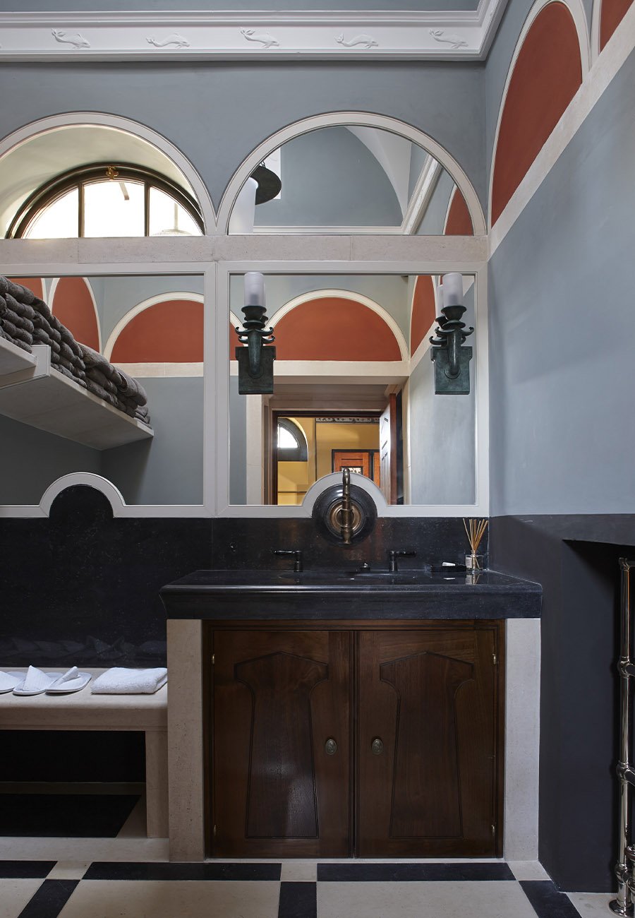 Washroom interior with classical arches, bespoke timber cabinetry and marble surfaces within the Gloucestershire bath house.