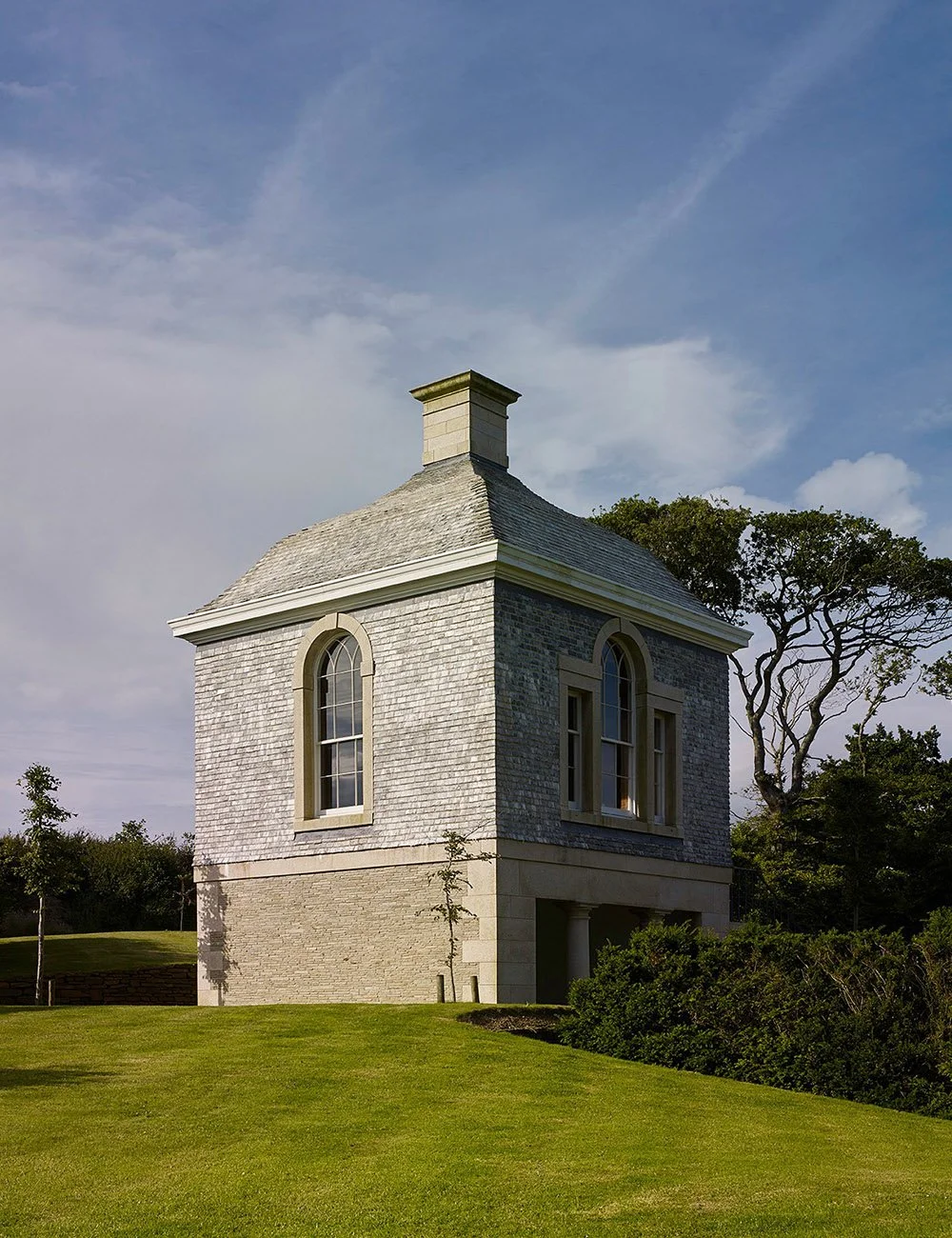 Classical garden pavilion in Cornwall viewed within a landscaped garden setting with mature trees and lawns.