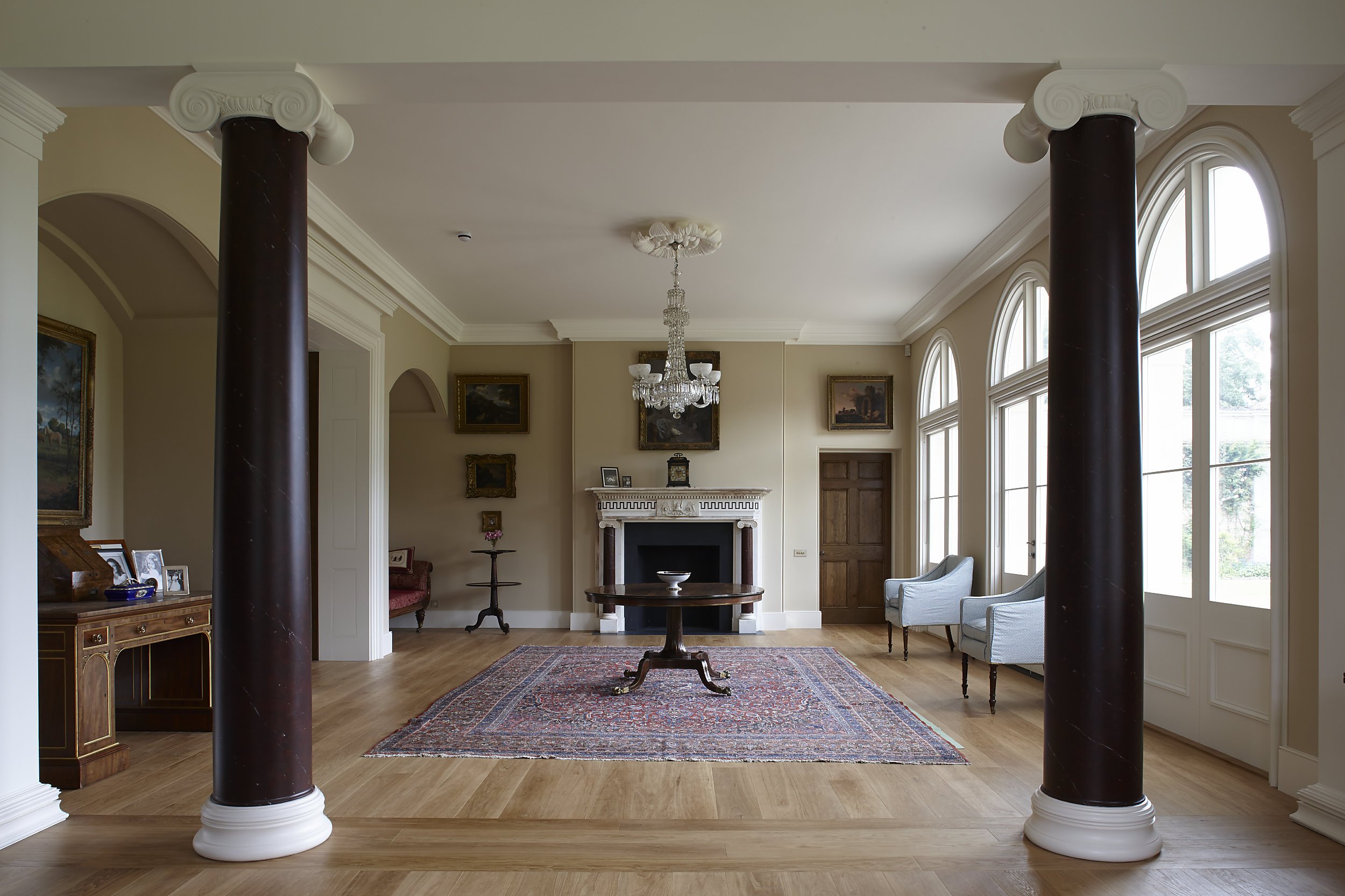 Classical drawing room interior with marble fireplace, chandelier, oak flooring and arched windows in a traditional country house