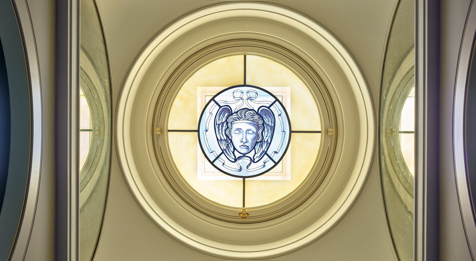Decorative stained glass oculus window within a historic London apartment, framed by classical mouldings and curved architectural detailing.