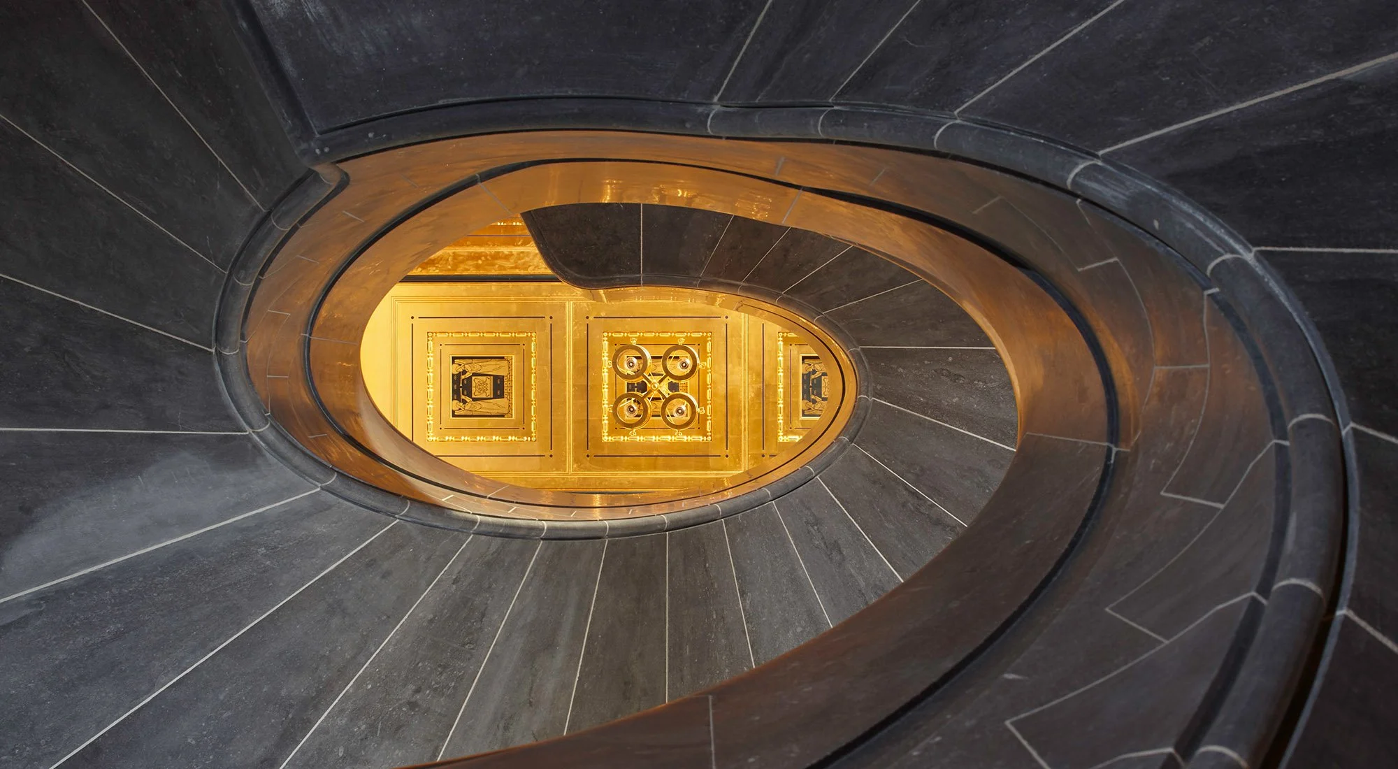 Spiral stone staircase detail within The Chapel of Christ the Redeemer at Culham featuring classical geometry and illuminated ceiling panels.