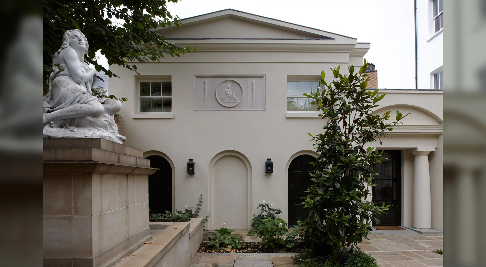 Classical London courtyard house with rendered façade, arched openings, stone paving and sculptural garden feature by Craig Hamilton Architects.