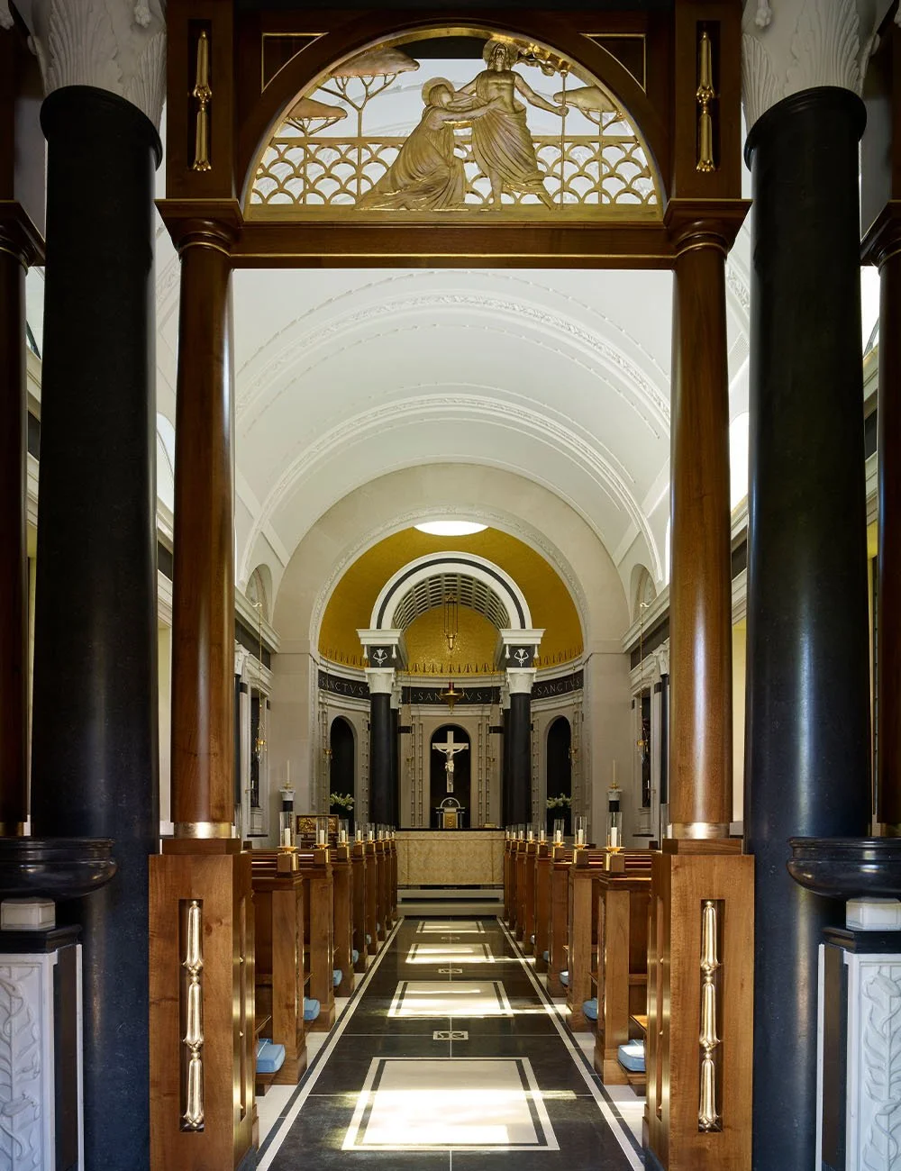View along the nave of the Chapel of Our Lady at Williamstrip showing classical columns, timber pews and vaulted ceilings.