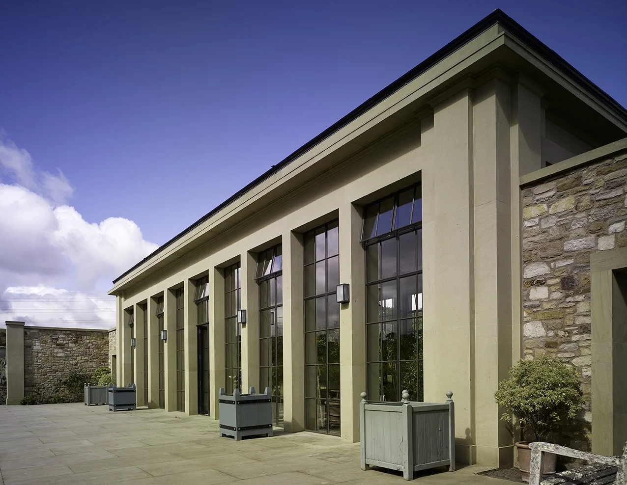 Detail of the orangery façade showing tall steel-framed glazing, classical proportions and natural stonework.