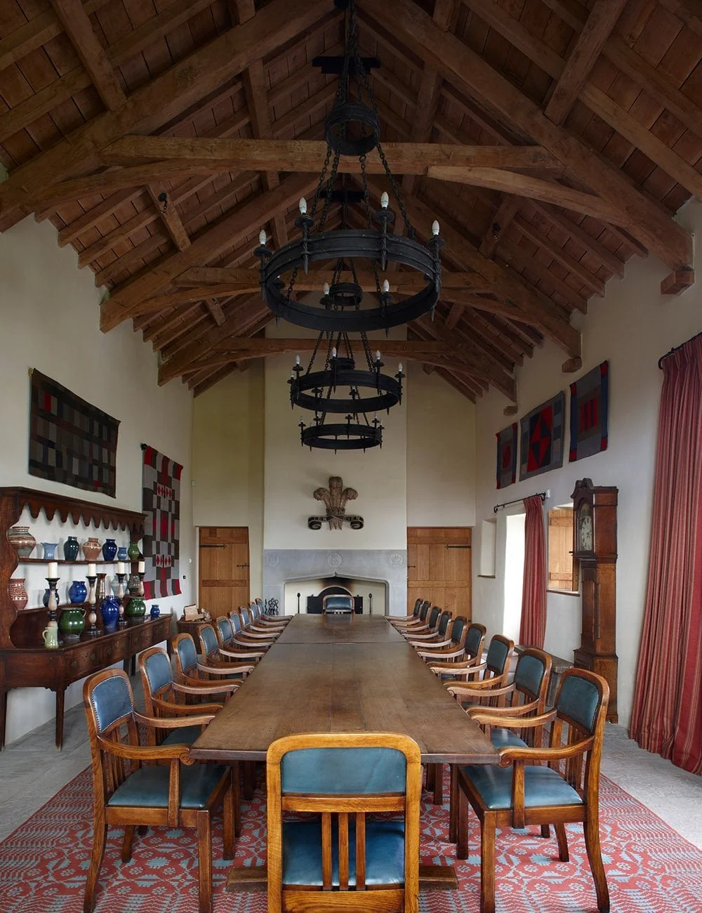 Dining hall with exposed timber roof and long oak table within the restored Llwynwermod country house.