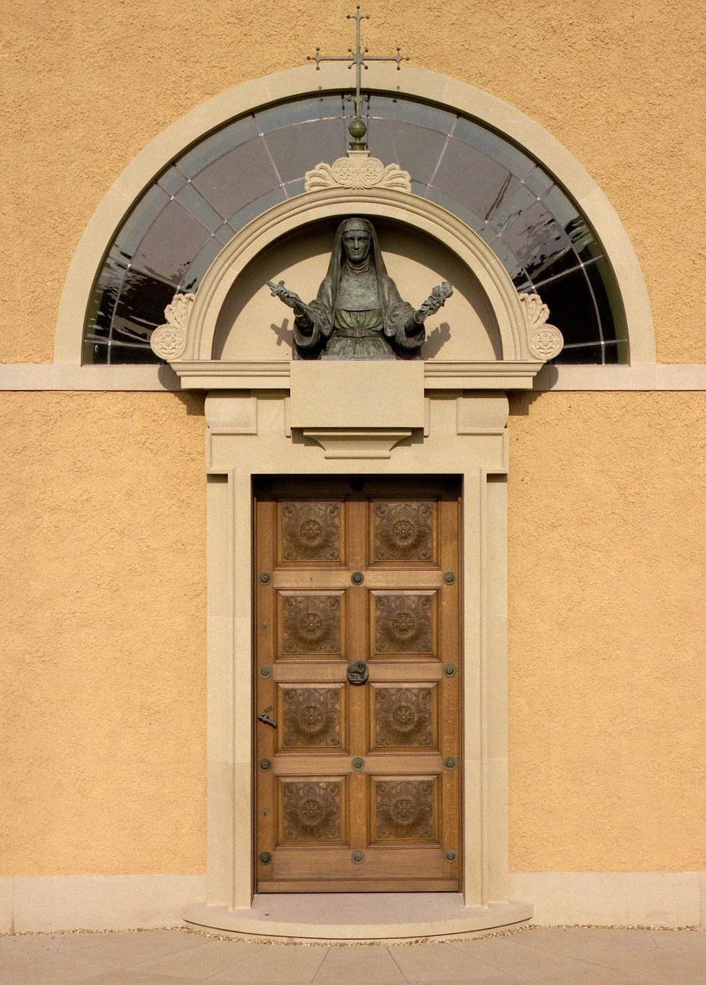 Classical entrance portal of a private Catholic chapel featuring carved timber doors, architectural mouldings, and a religious sculpture above the entrance.
