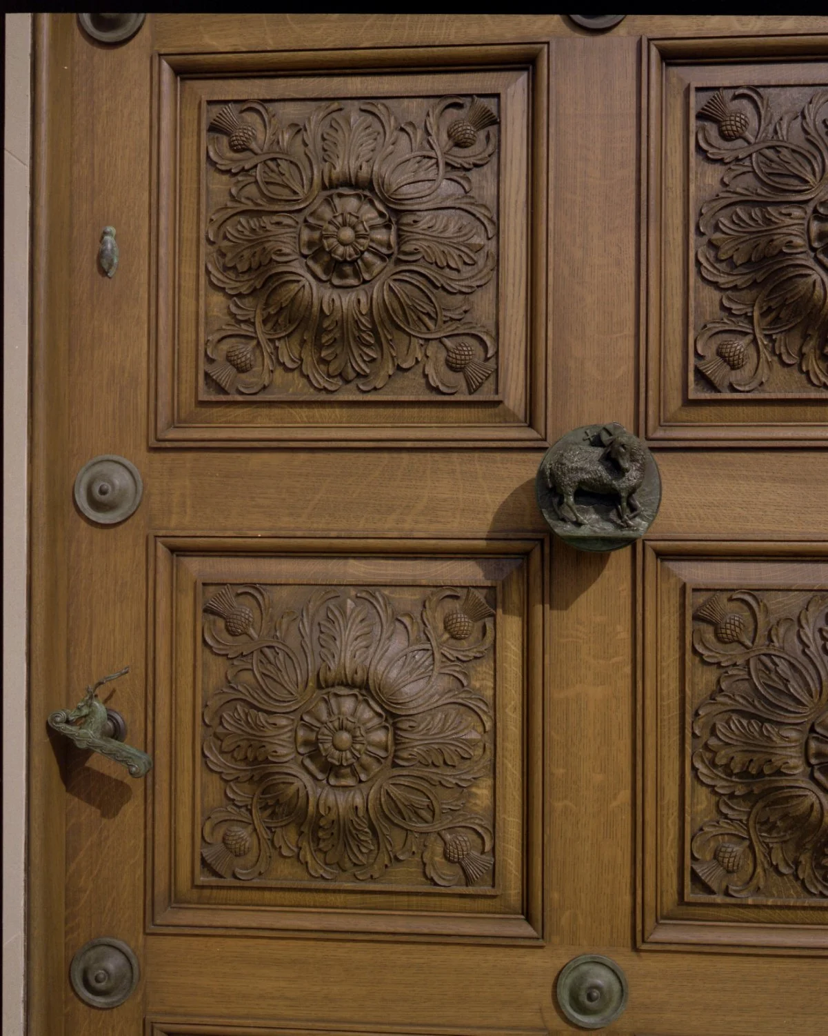 Detail of the chapel’s handcrafted timber entrance doors featuring carved floral panels and traditional ironmongery.