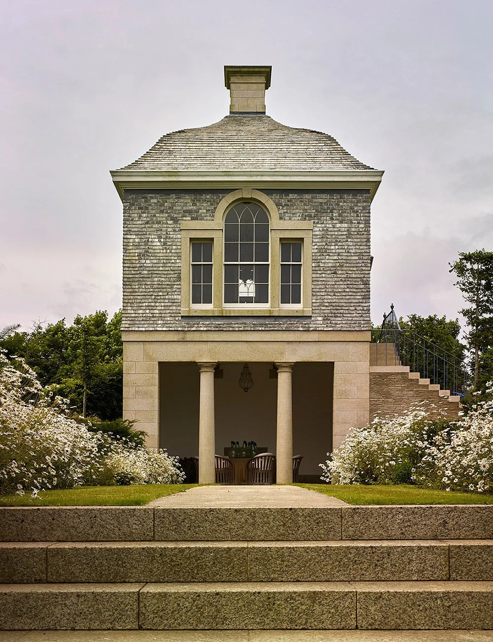 Front elevation of a classical garden pavilion in Cornwall with stone columns, arched window and formal planting.