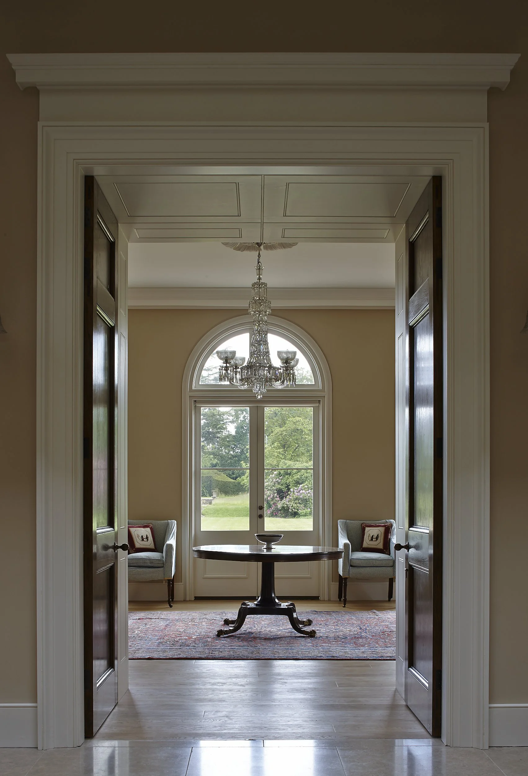 Symmetrical interior view through classical doorway towards arched window and chandelier in a traditional country house